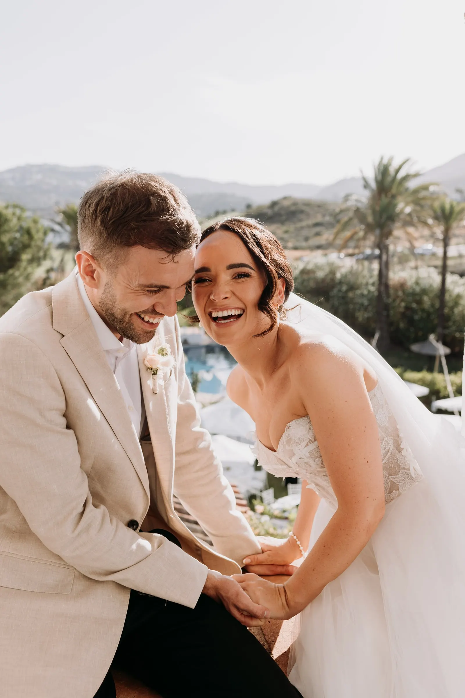 Bride and groom laughing together on the tower ledge above the garden, Hacienda San José