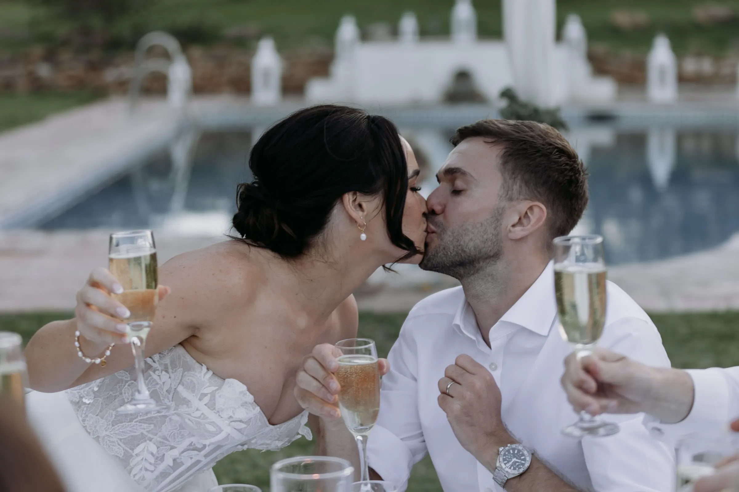 Bride and groom kissing with glasses of cava by the pool, Hacienda San José