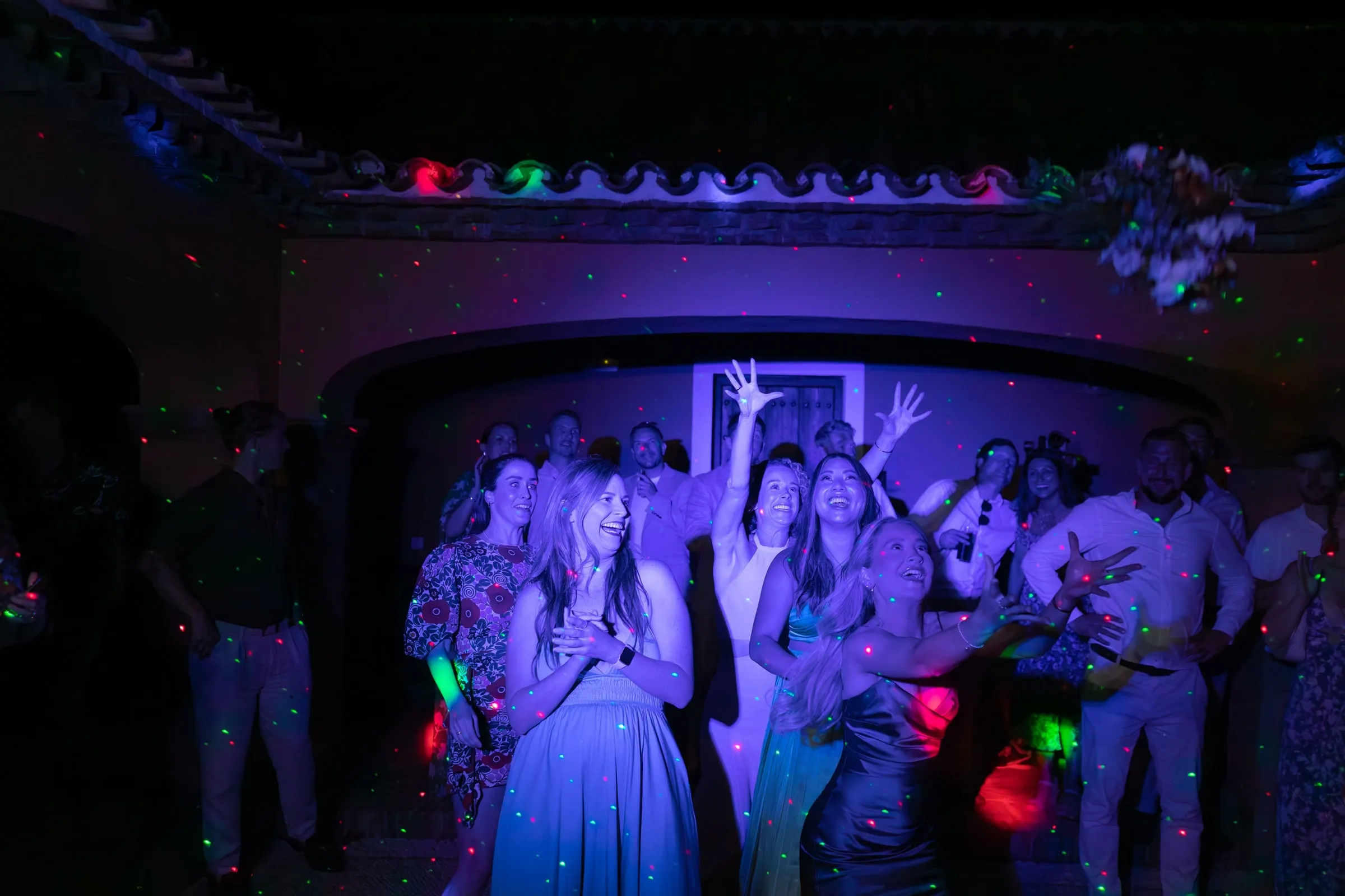 Guests dancing with their arms up under purple and blue party lights, Hacienda San José