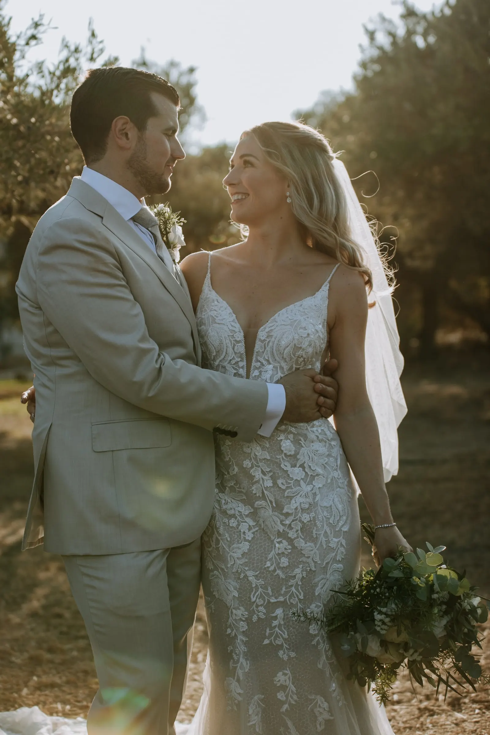 Los novios abrazados con la luz dorada de la tarde entre olivos, ramo en mano, Hacienda San José, Mijas