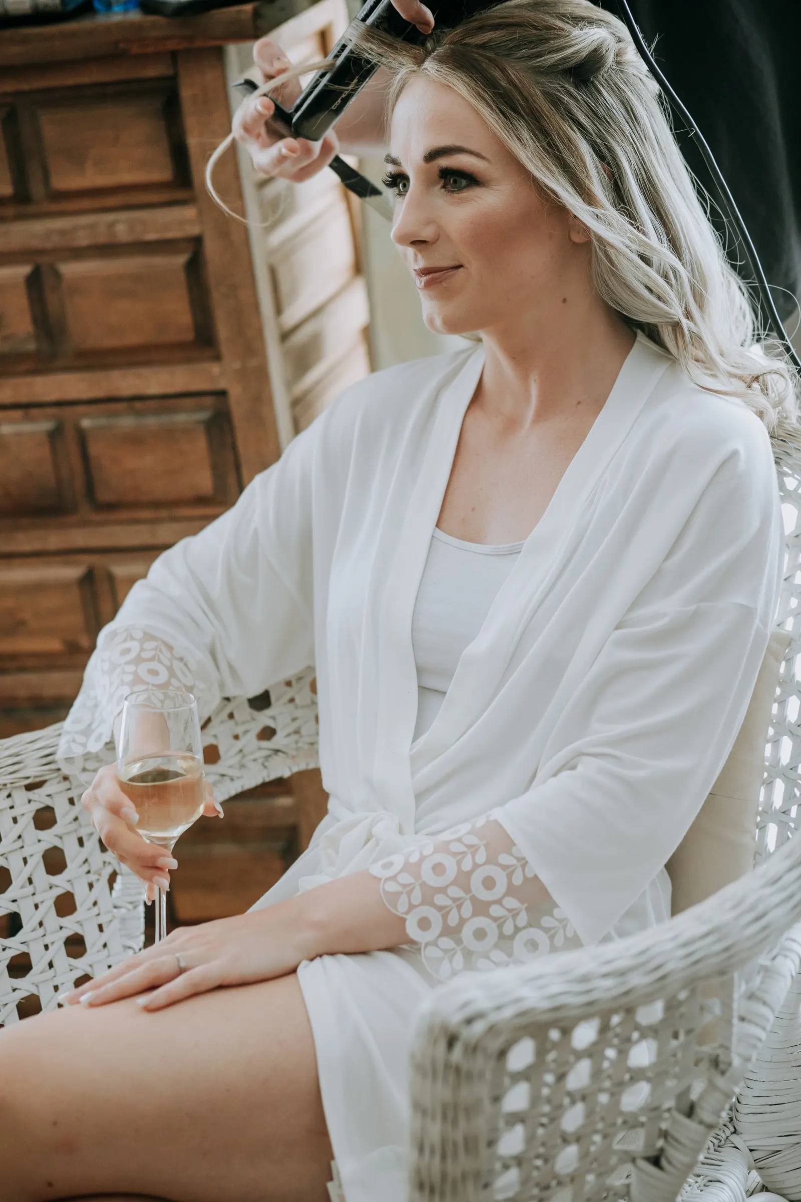 La novia, en bata blanca y con una copa de vino, mientras la peinan, Hacienda San José, Mijas