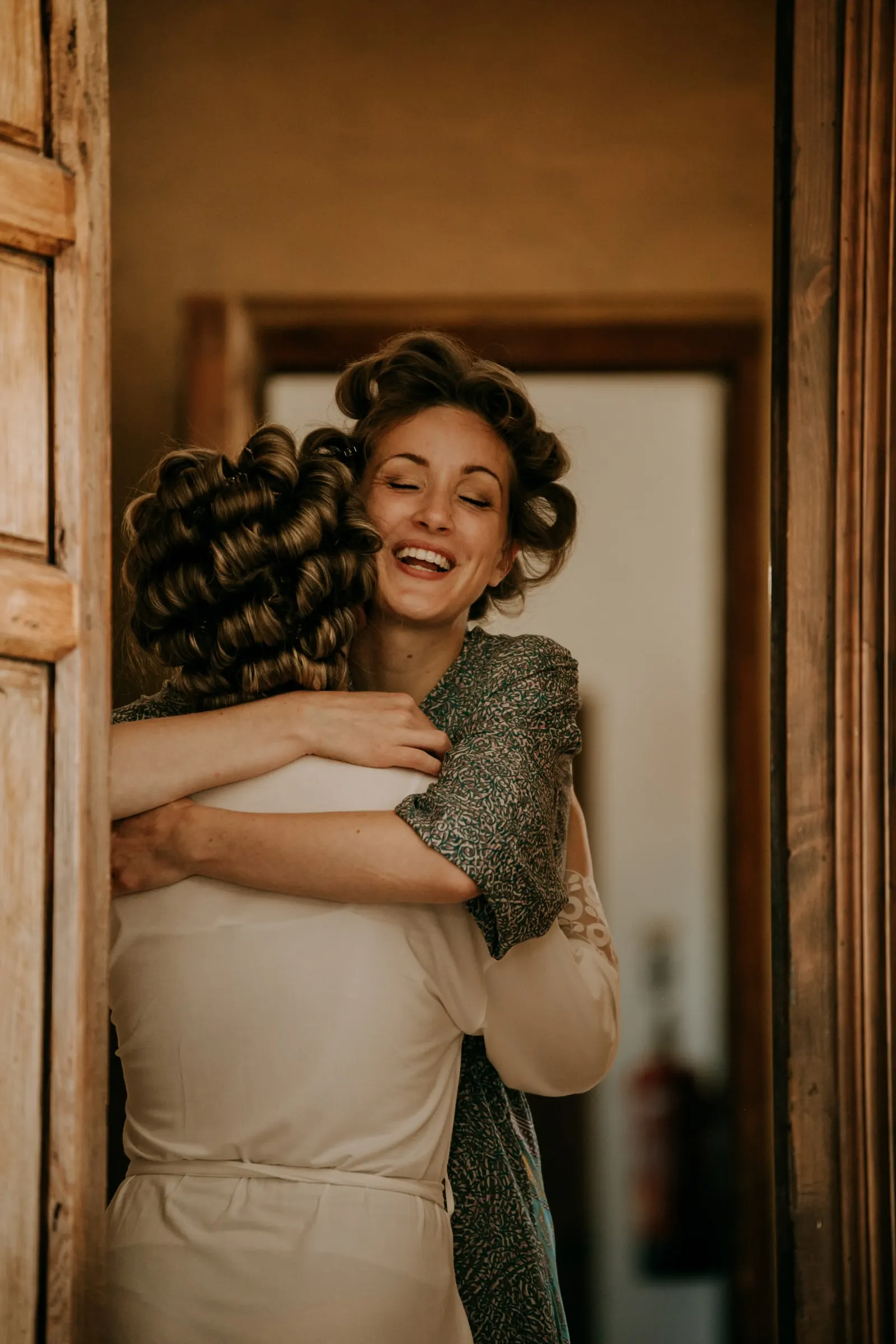 Dos mujeres con rulos se dan un abrazo cariñoso en el marco de una puerta de madera, Hacienda San José, Mijas