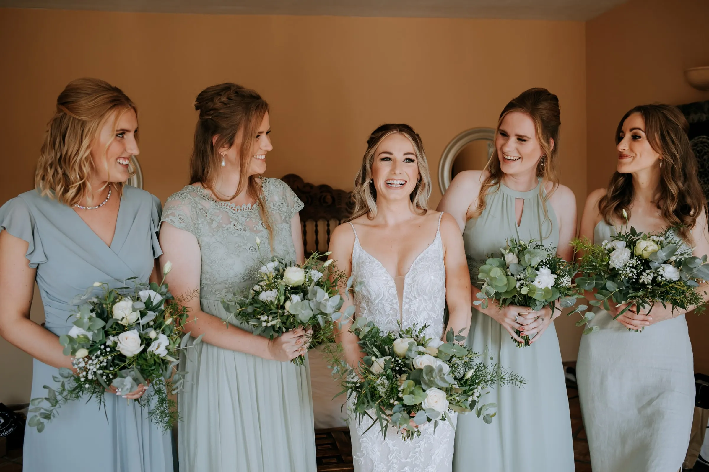 La novia ríe con cuatro damas de verde salvia y azul, todas con ramos blancos, Hacienda San José, Mijas
