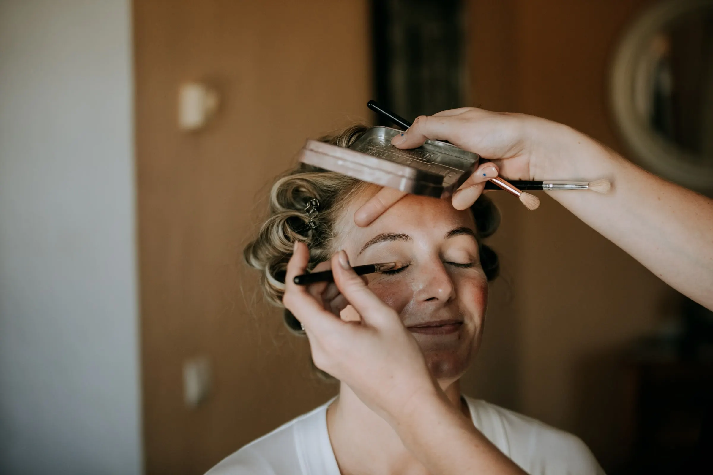 Primer plano del pincel de la maquilladora sobre el párpado de una mujer con rulos que sonríe, Hacienda San José, Mijas
