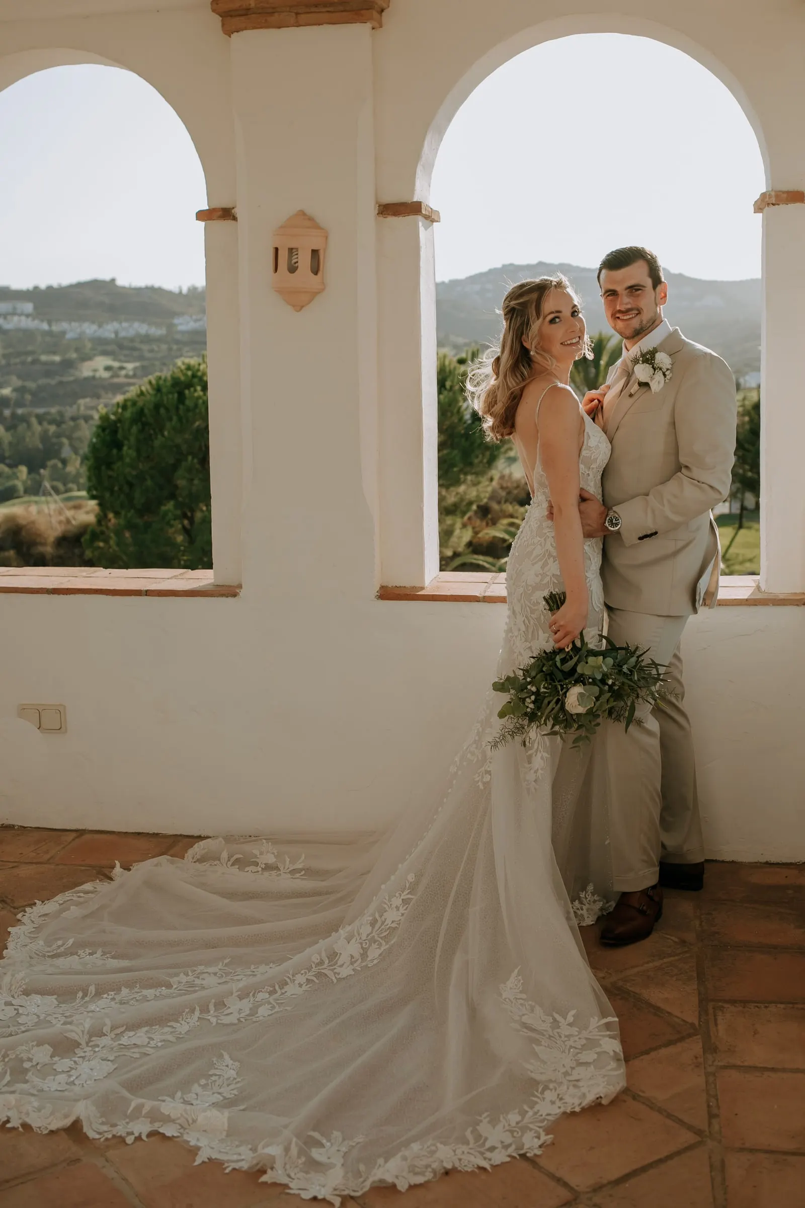 Los novios enmarcados por un arco blanco, con la cola de encaje sobre el suelo de barro, Hacienda San José, Mijas