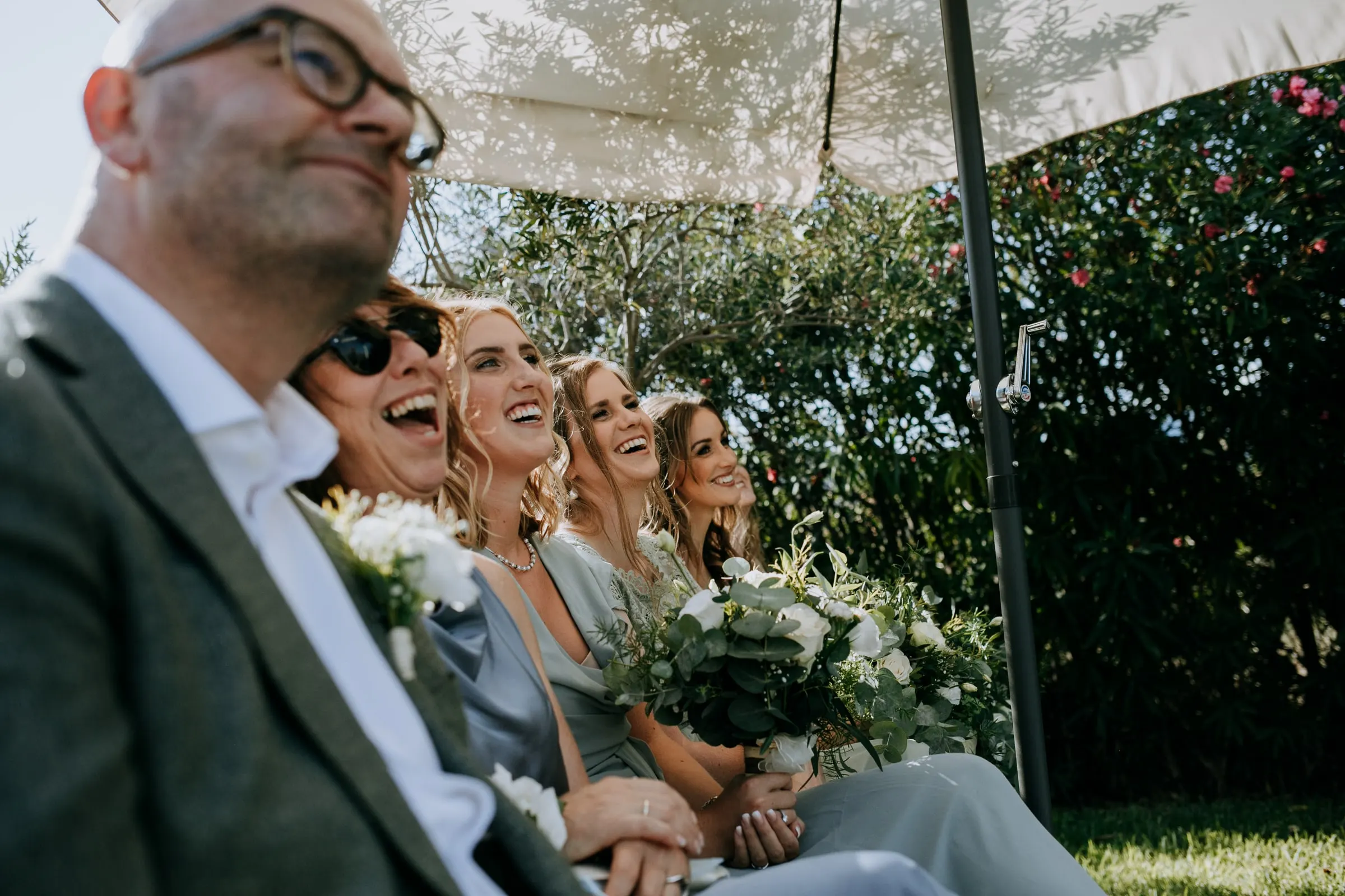 Invitados y damas de honor ríen en la primera fila durante la ceremonia, Hacienda San José, Mijas