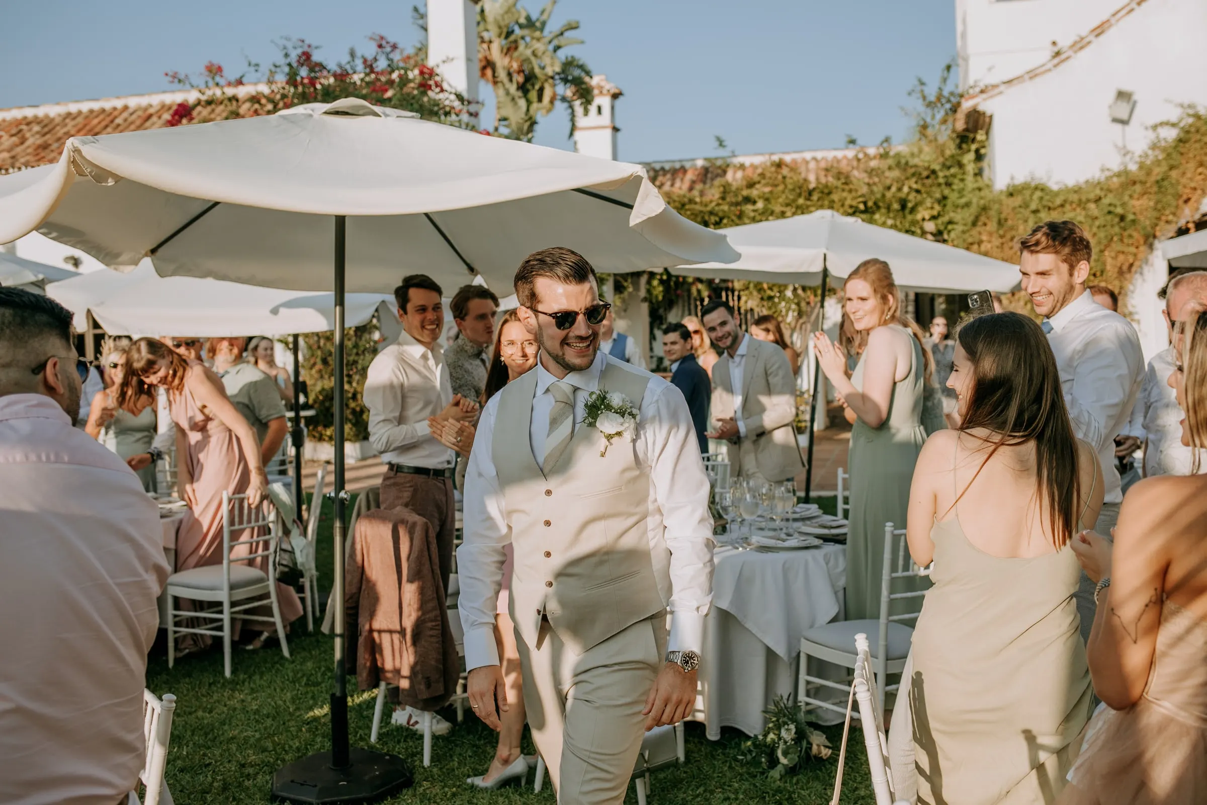 El novio, con gafas de sol y chaleco, camina entre los invitados en el cóctel del jardín, Hacienda San José, Mijas
