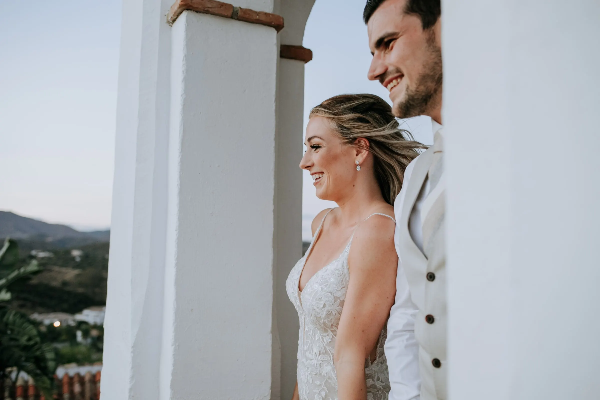 Los novios sonríen juntos en una terraza blanca al anochecer, con las colinas detrás, Hacienda San José, Mijas