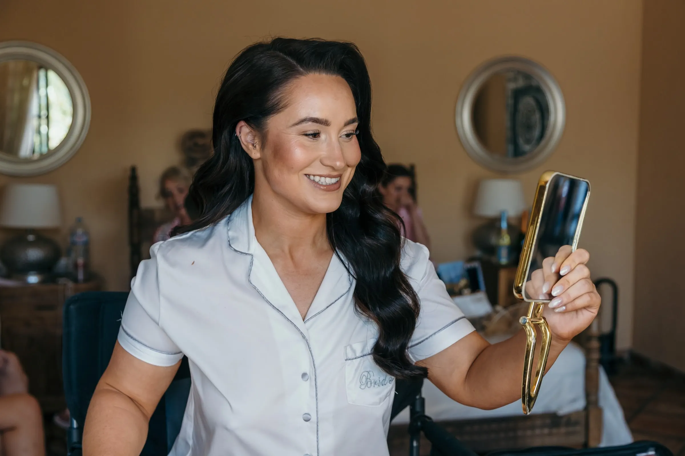 Bride in a white robe, hair and make-up done, smiling at a hand mirror, Hacienda San José, Mijas