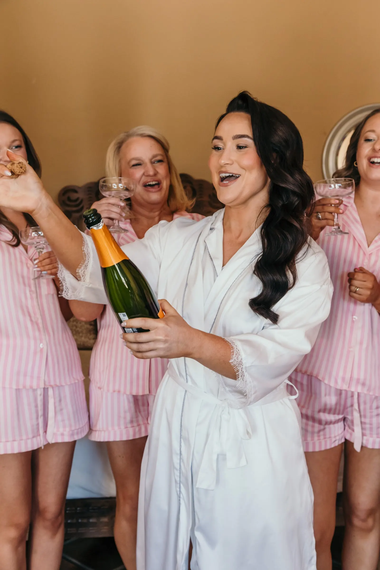 La novia descorcha el champán entre damas con pijamas de rayas rosas
