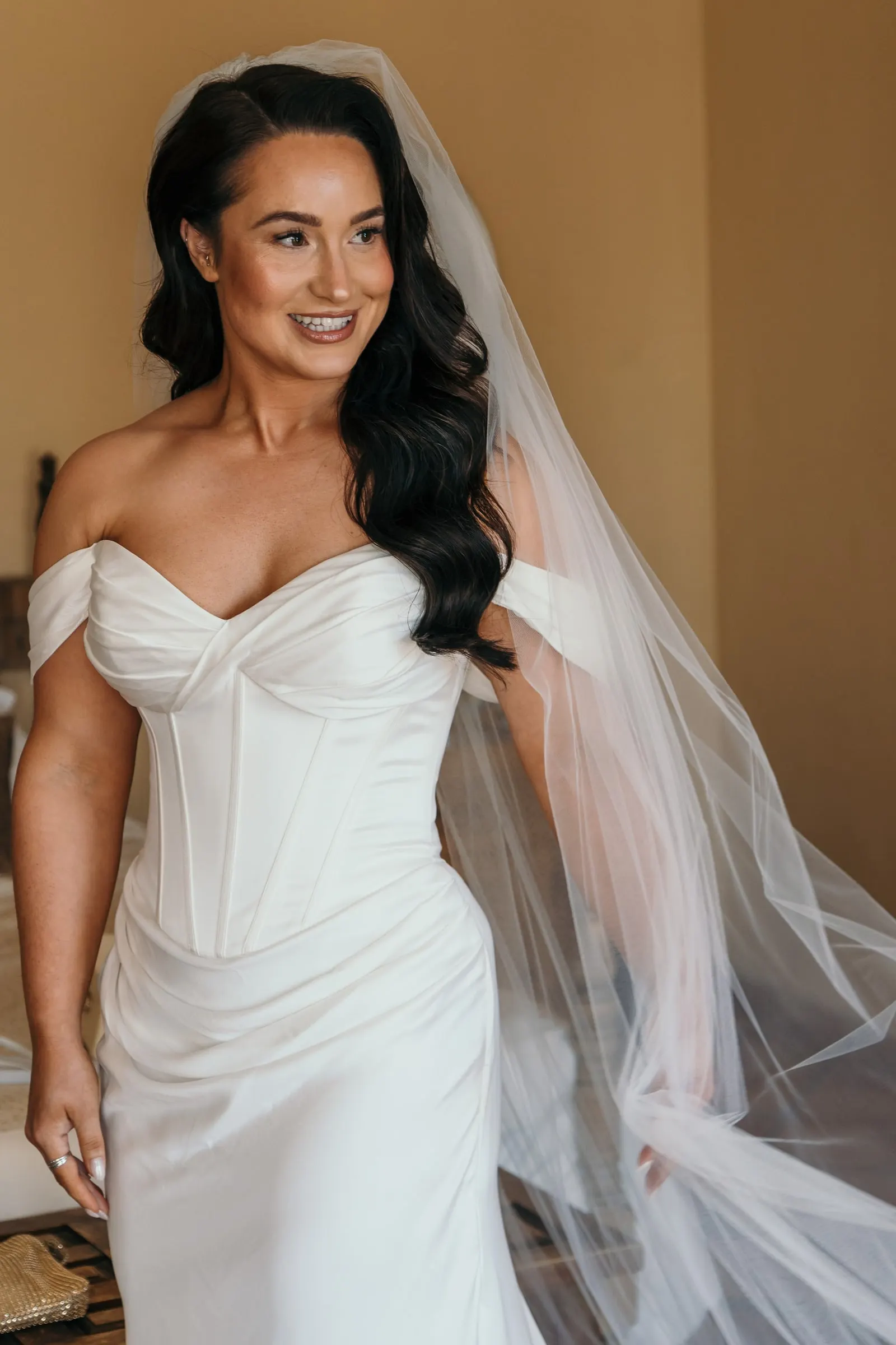 La novia, con vestido de corsé y velo largo, sonríe en una habitación soleada