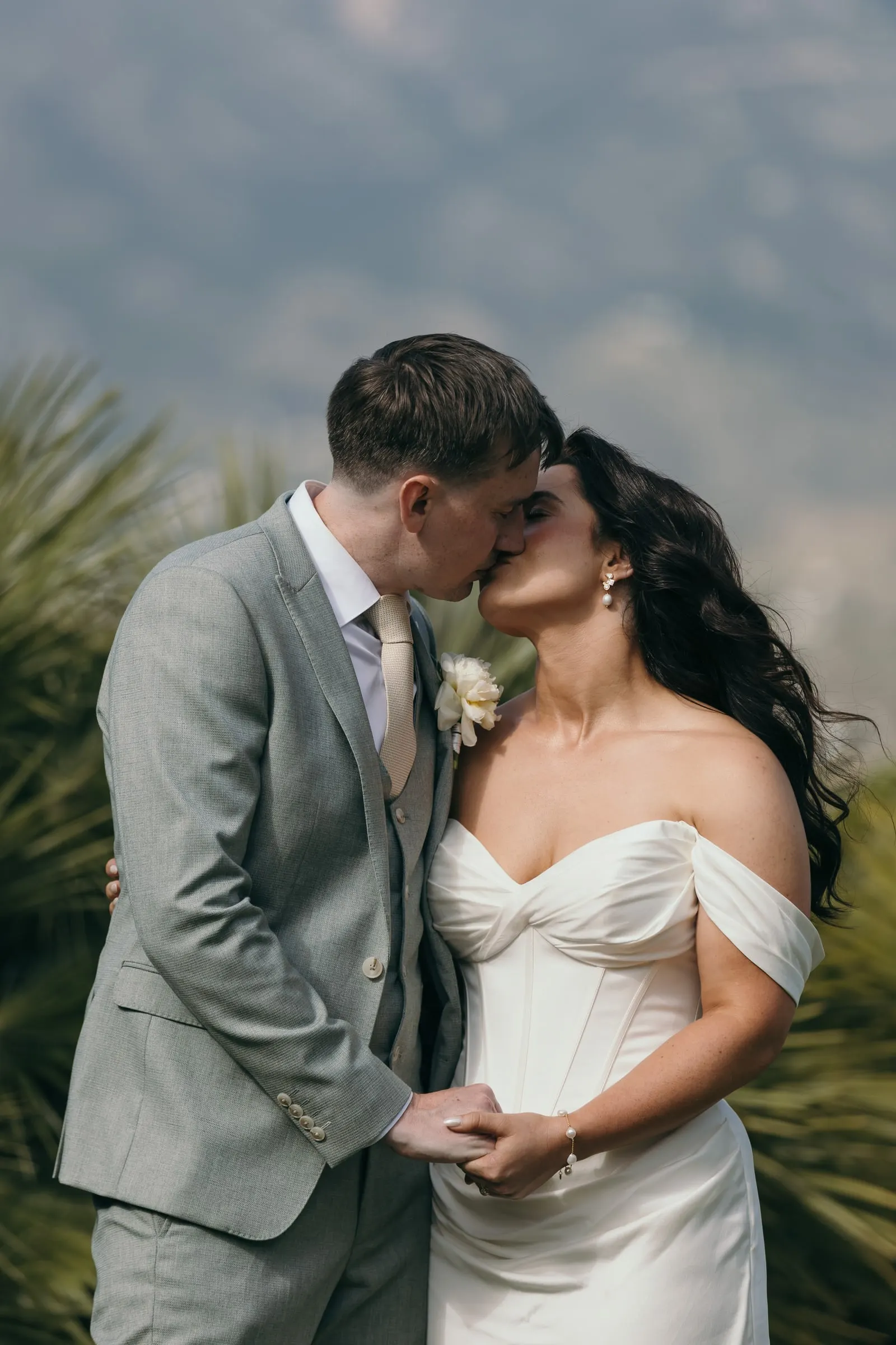Los novios se besan entre hojas de palmera con las montañas desenfocadas