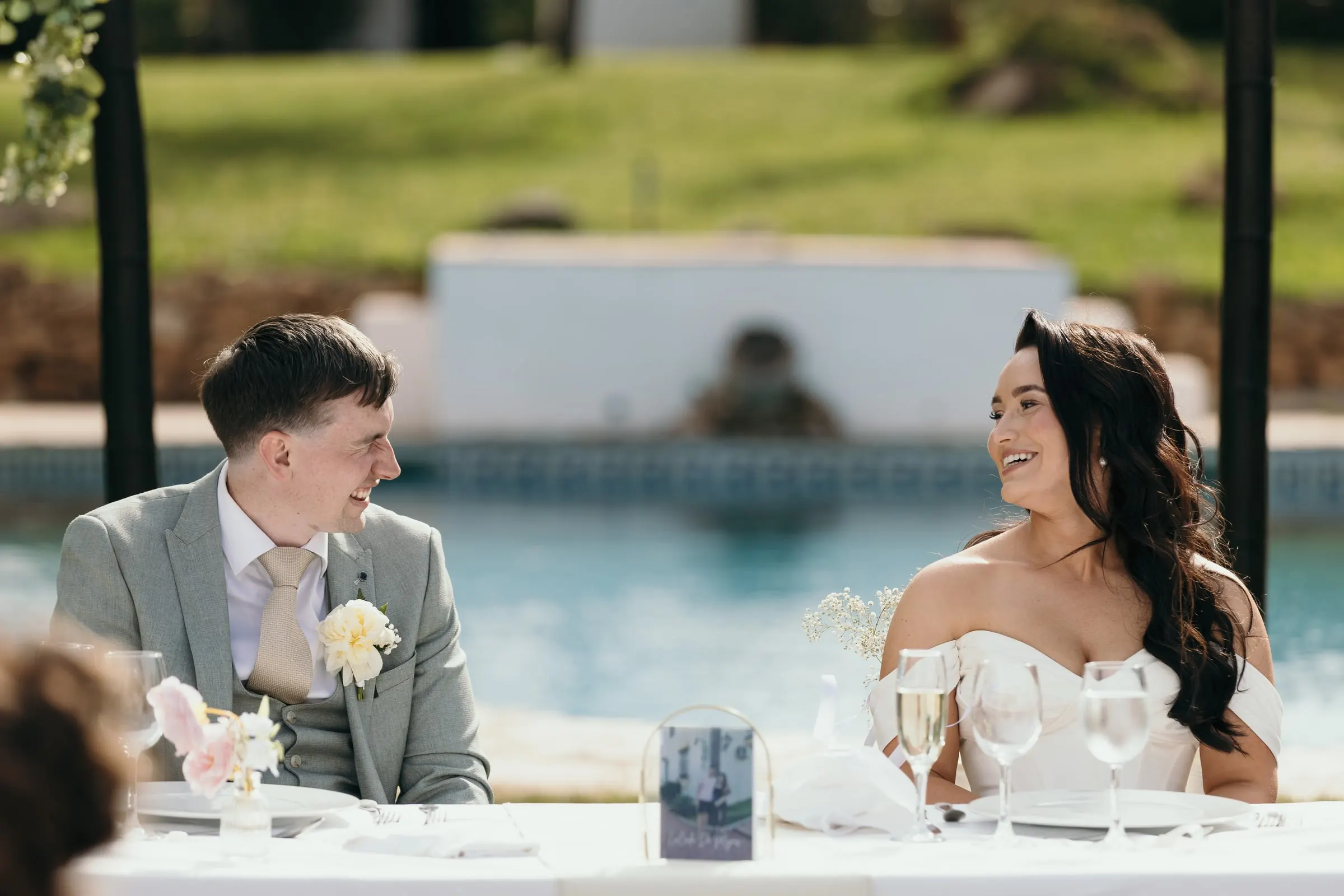 Los novios ríen en la mesa presidencial con la piscina detrás, Mijas