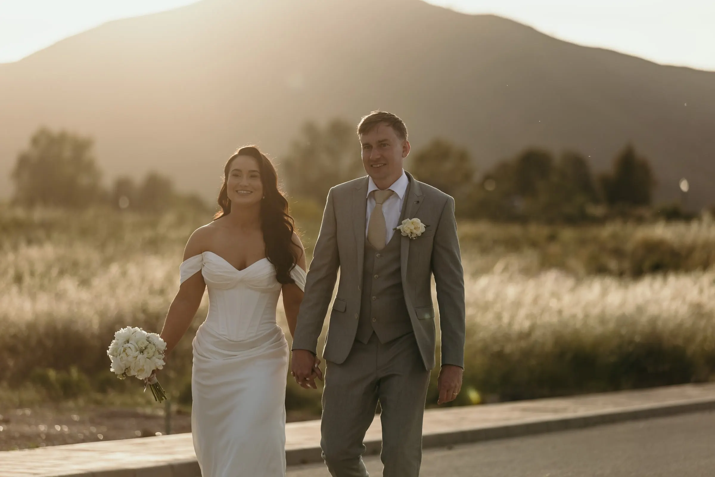 Los recién casados pasean por un camino tranquilo con la luz de la tarde