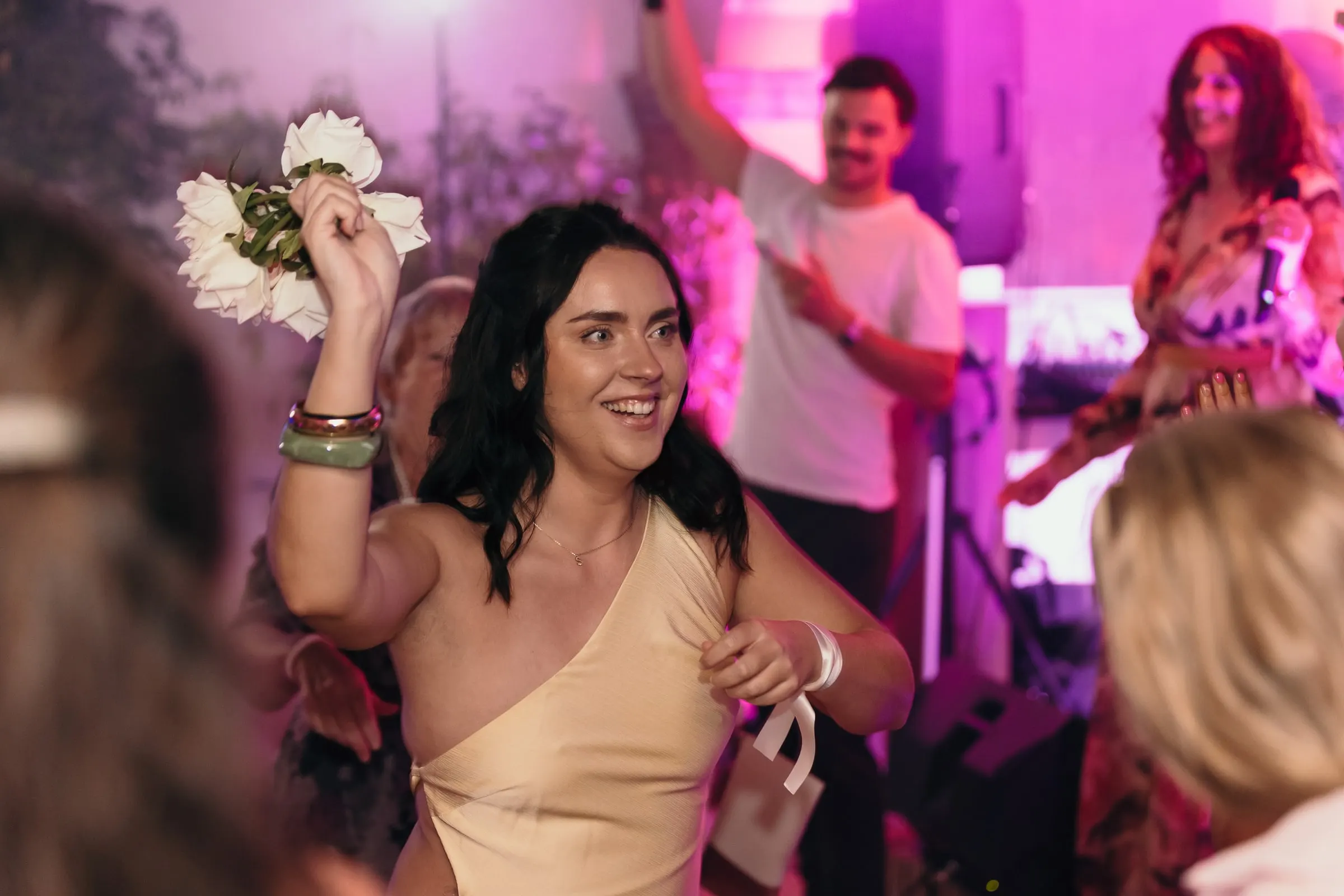 Una invitada agita el ramo de la novia en la pista bajo luz rosa