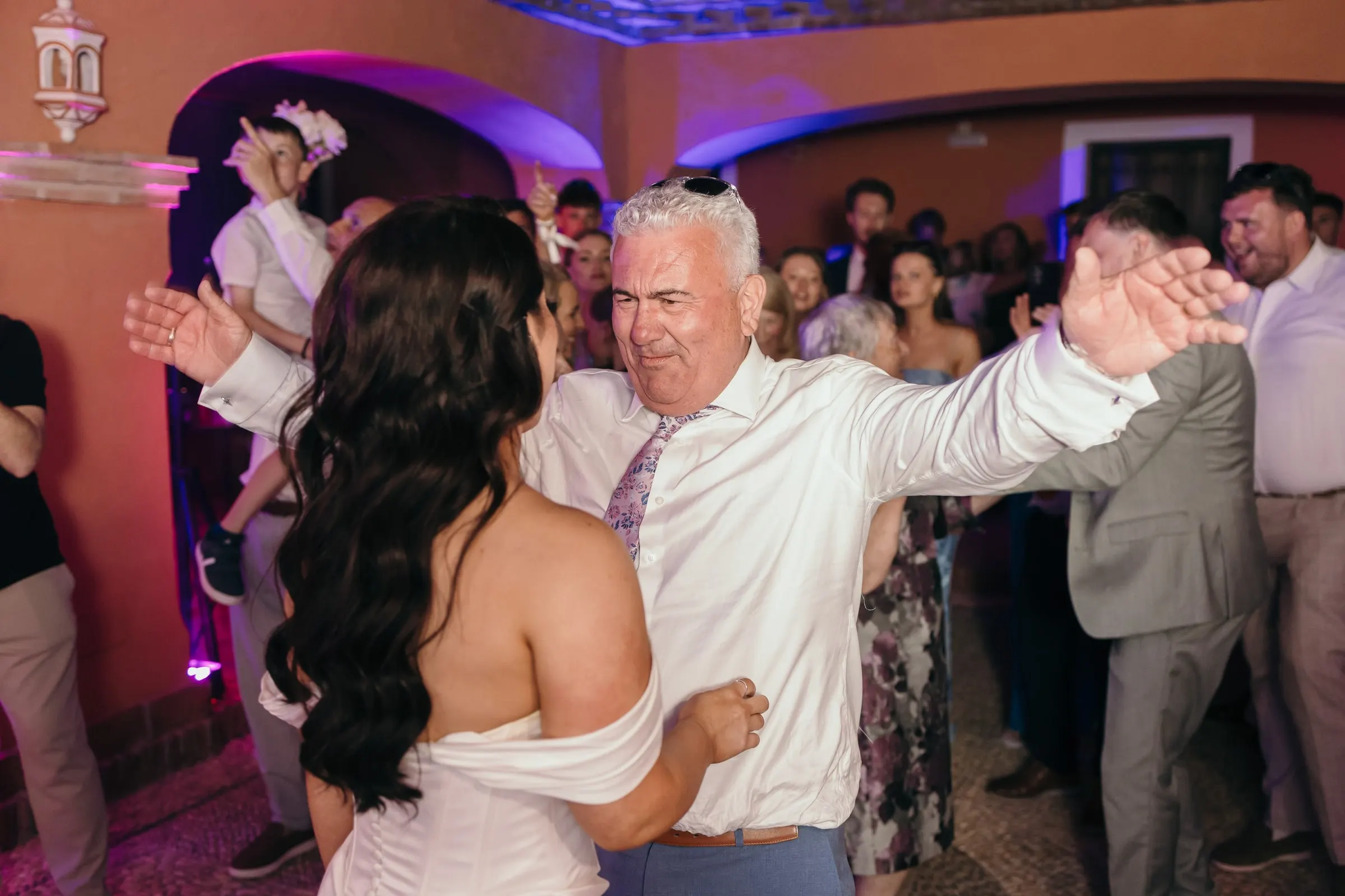 Un hombre de camisa blanca baila con los brazos abiertos frente a la novia
