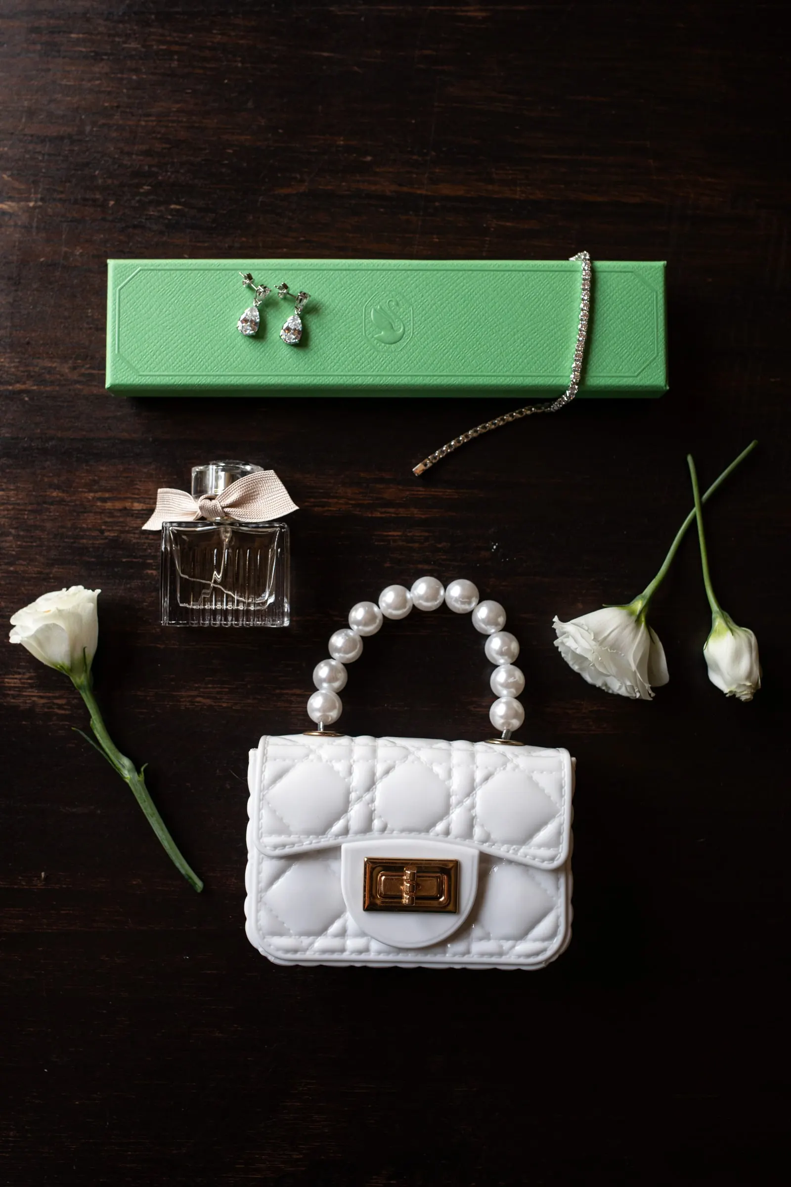 Pearl handbag, perfume, earrings and white roses laid out on dark wood before the wedding at Hacienda San José