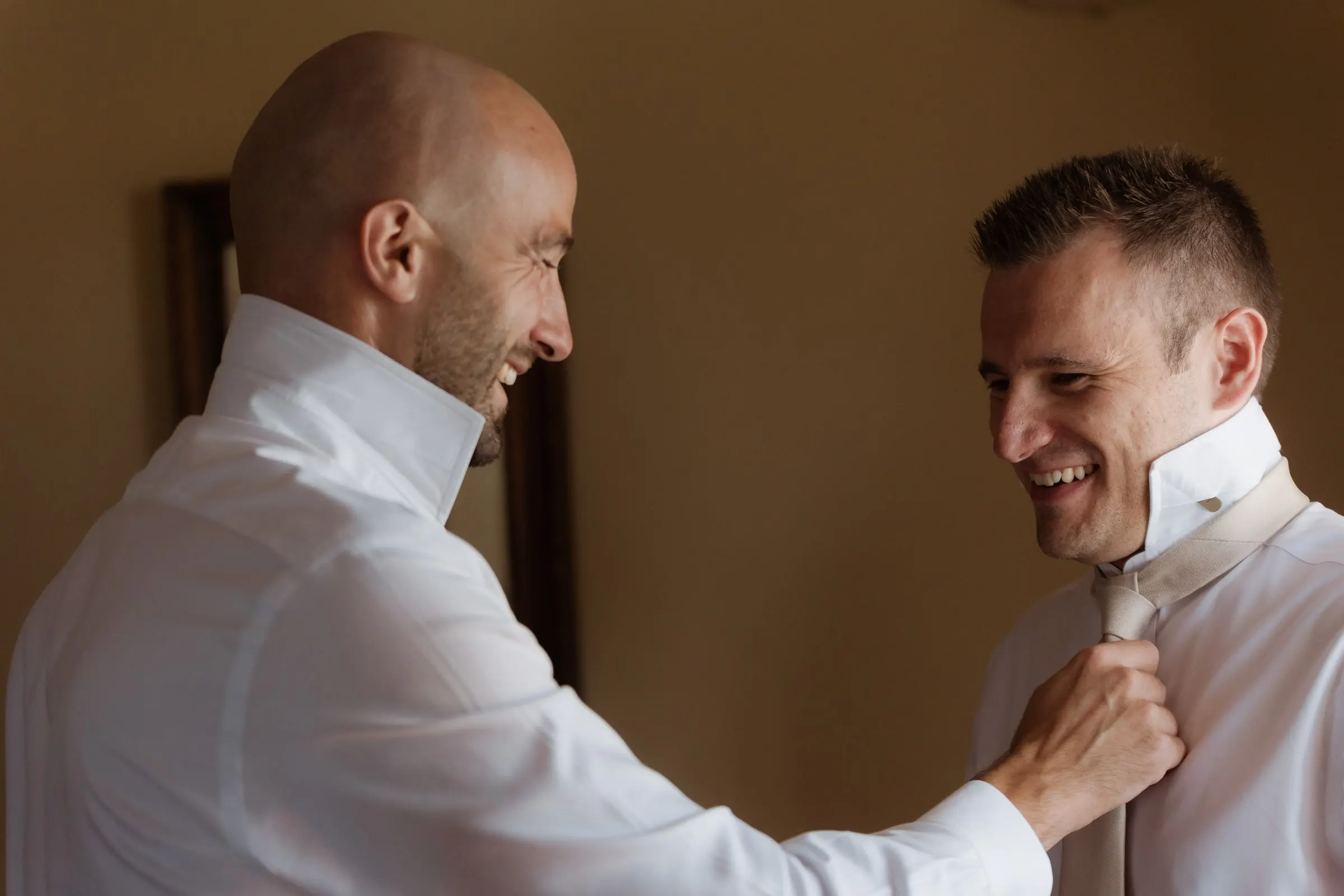Groomsman helping the groom with his tie, both laughing