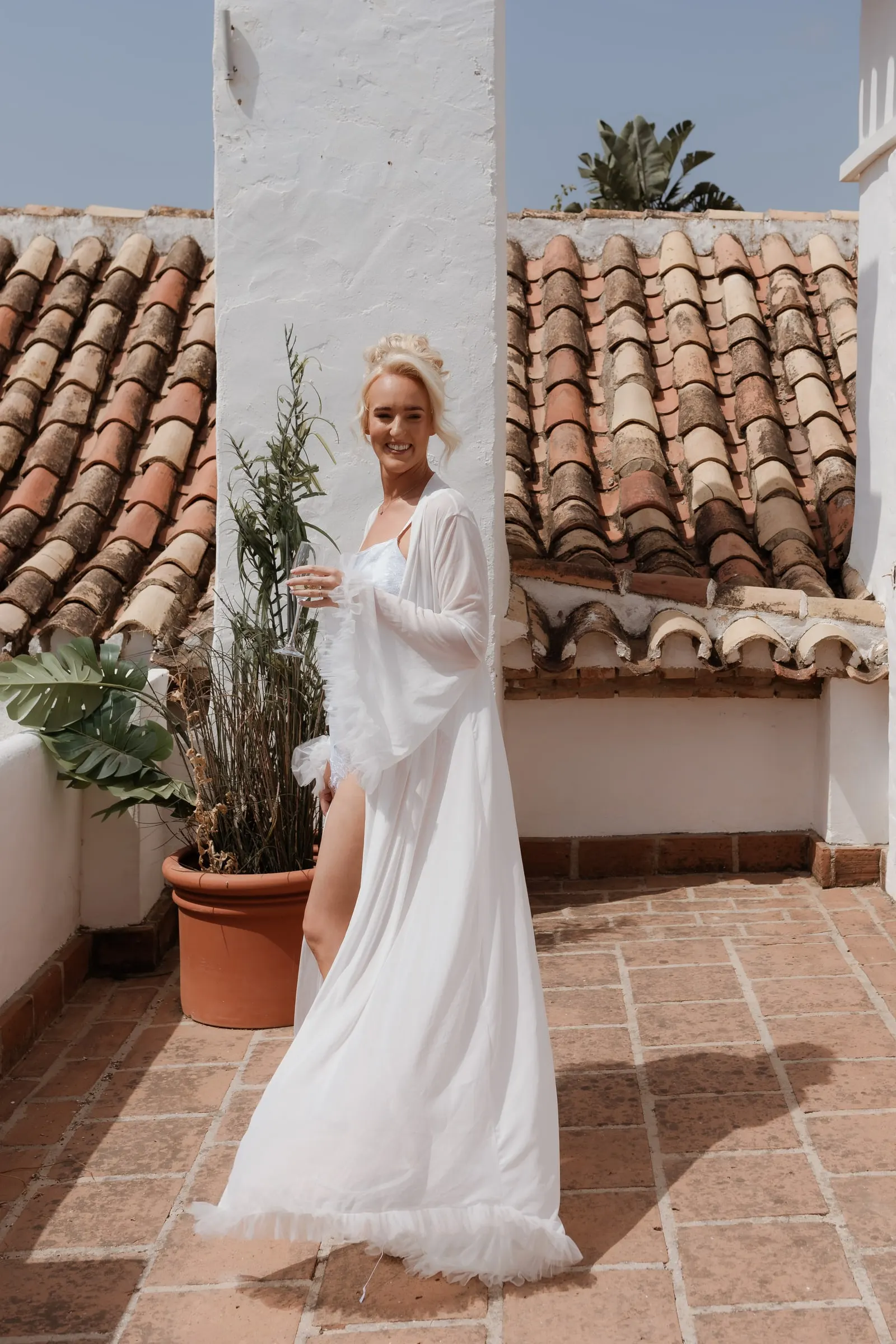 Bride in a long robe on a terrace among terracotta roofs and a white tower at Hacienda San José