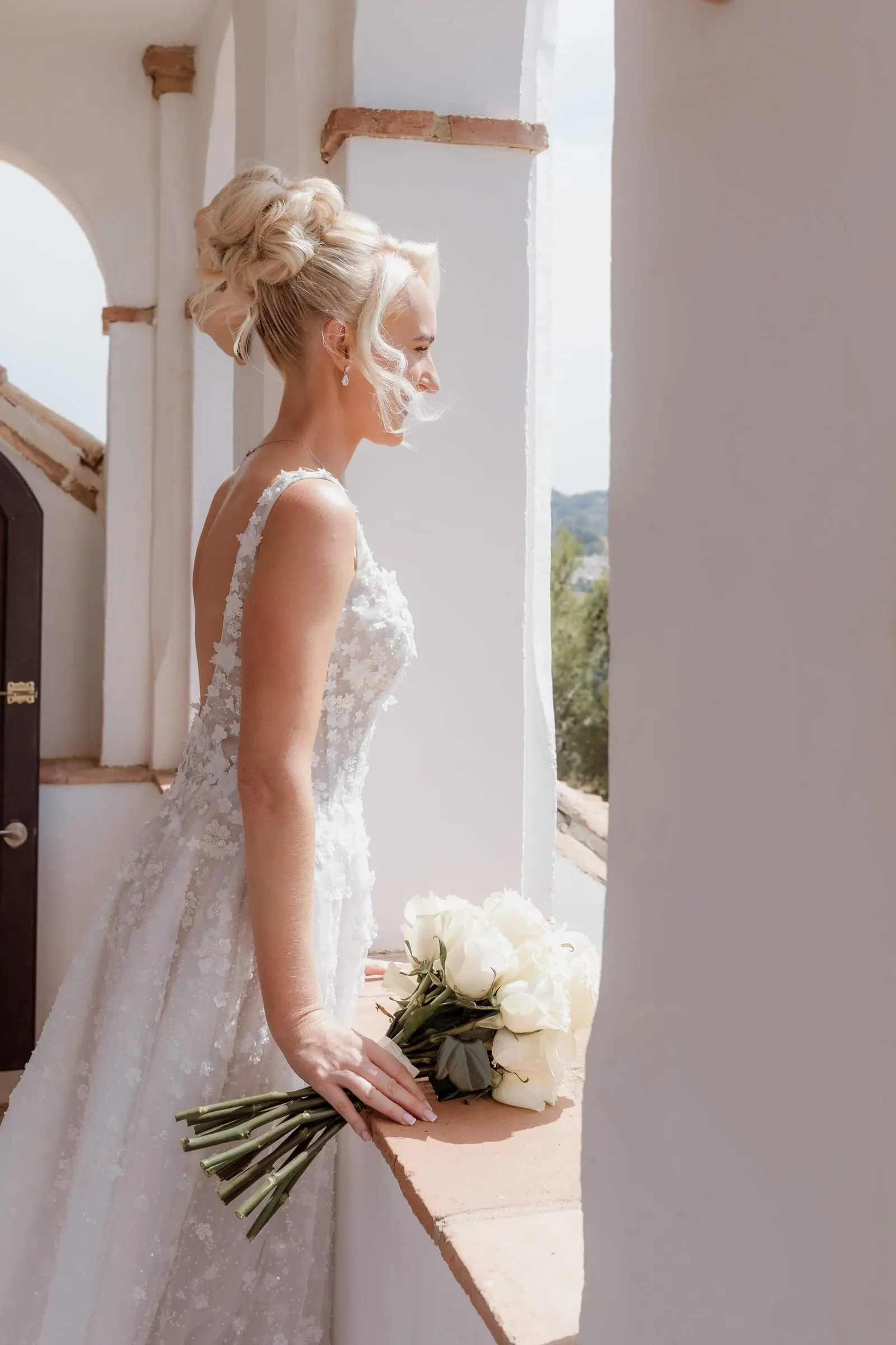 Bride in profile with her bouquet resting on a white windowsill, Mijas