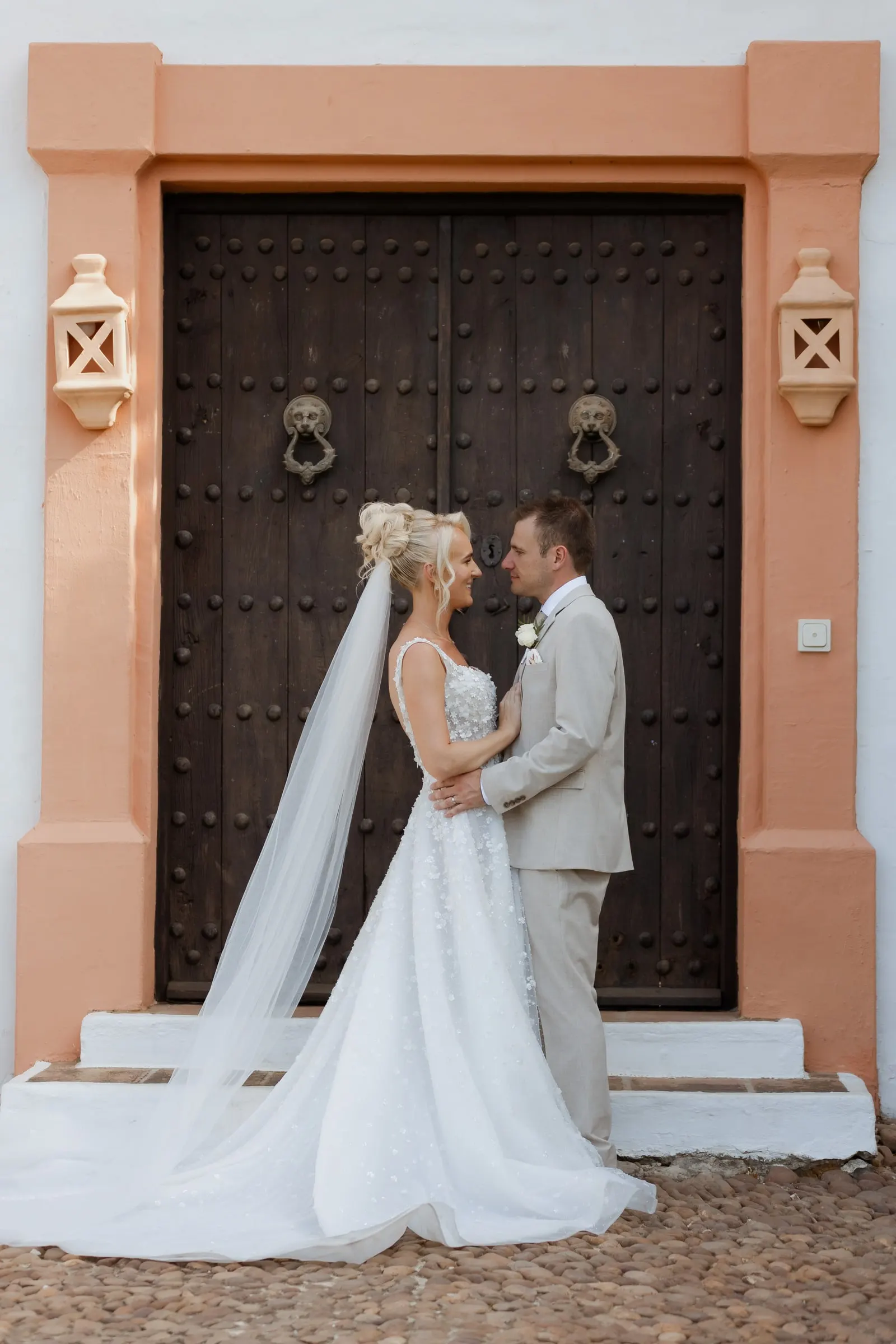 Bride and groom at a studded wooden door framed in terracotta, Mijas