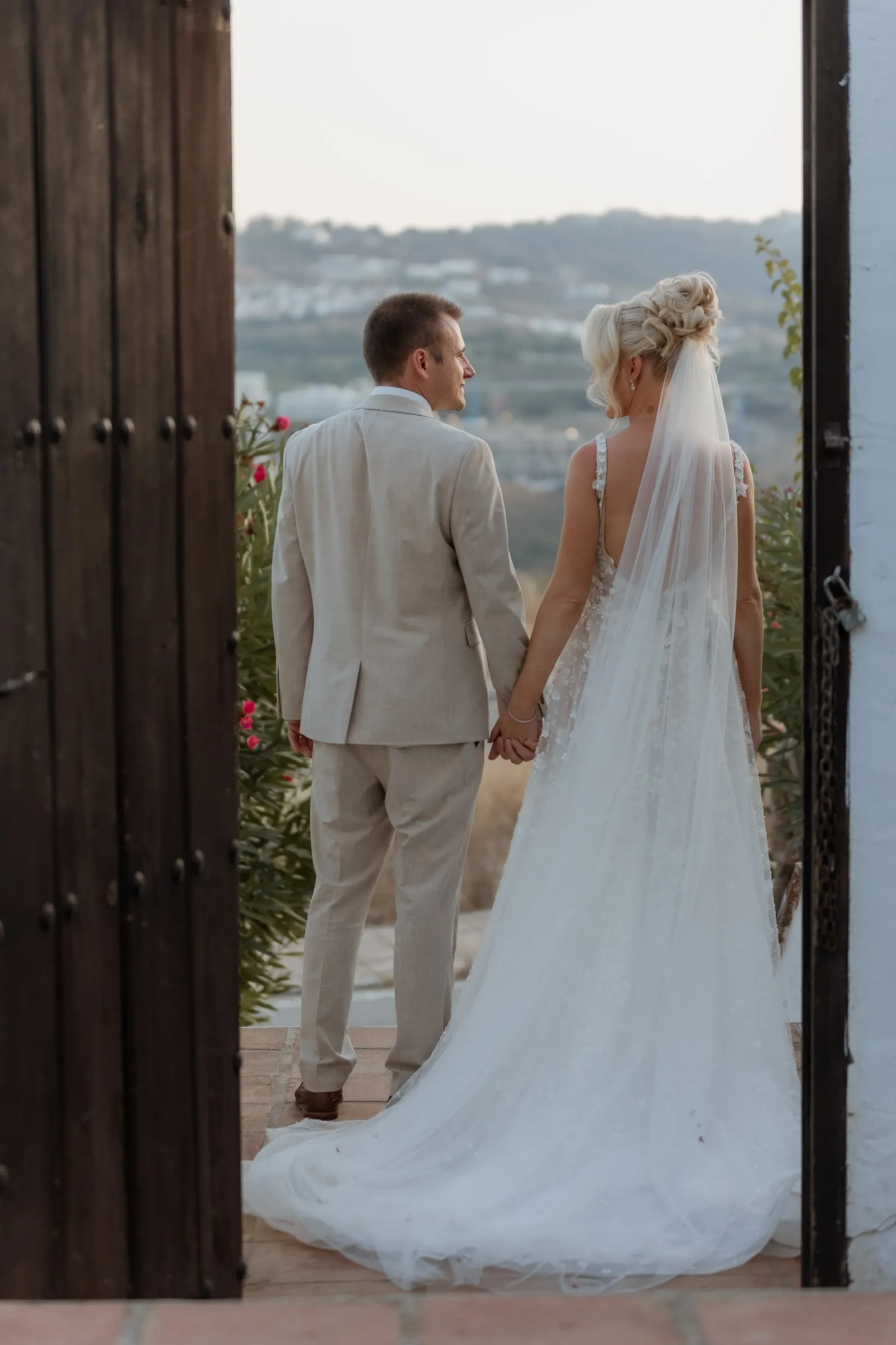 Bride and groom framed by a wooden doorway, looking out over the valley in Mijas