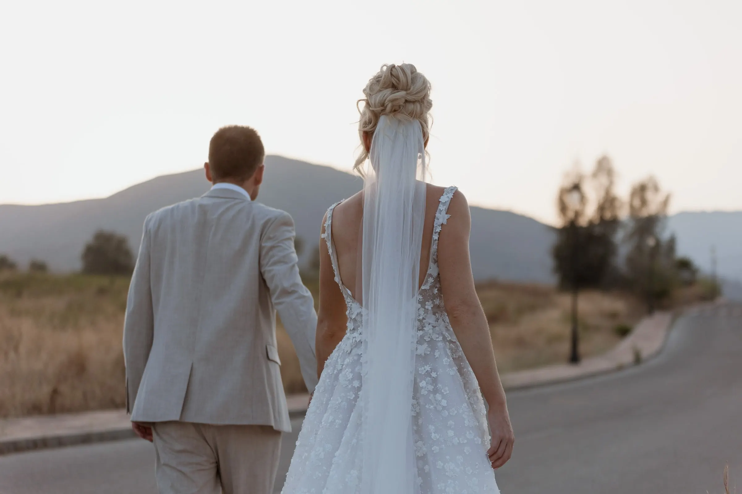 Los novios caminan por una carretera tranquila hacia los montes al atardecer