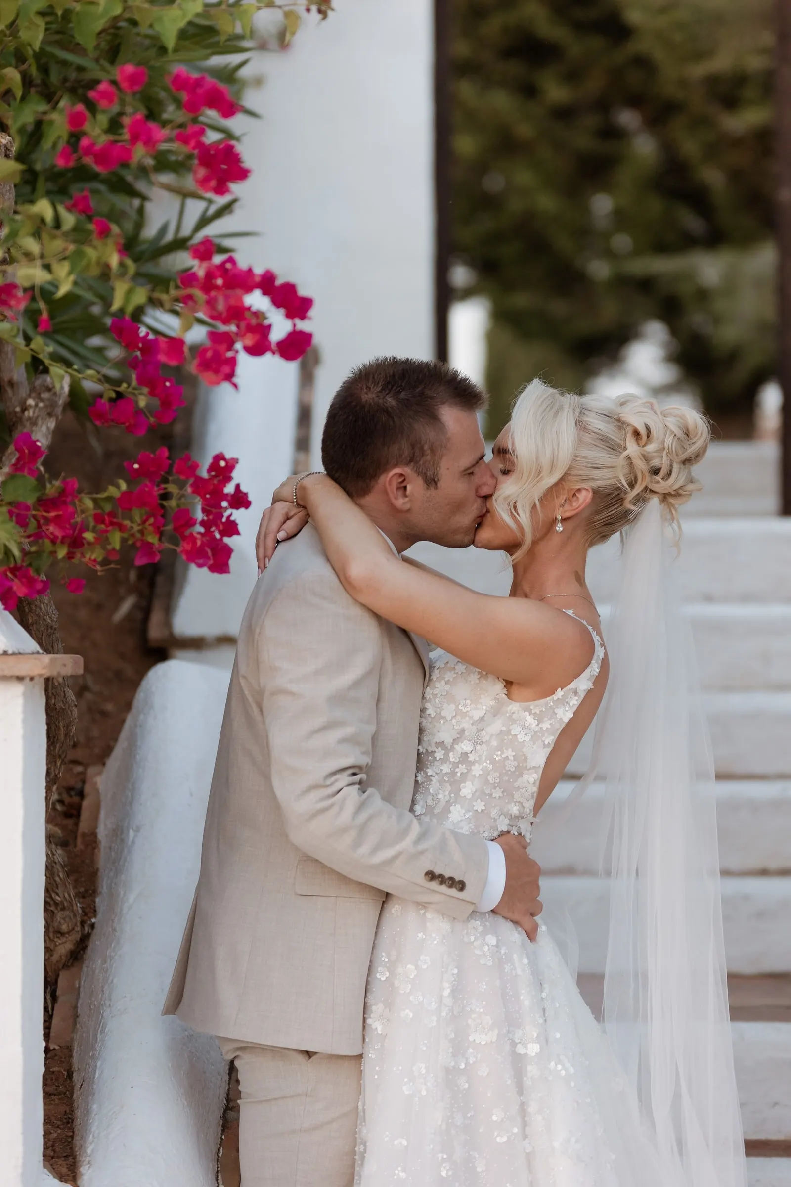 Couple kissing beside a white wall and bougainvillea at Hacienda San José