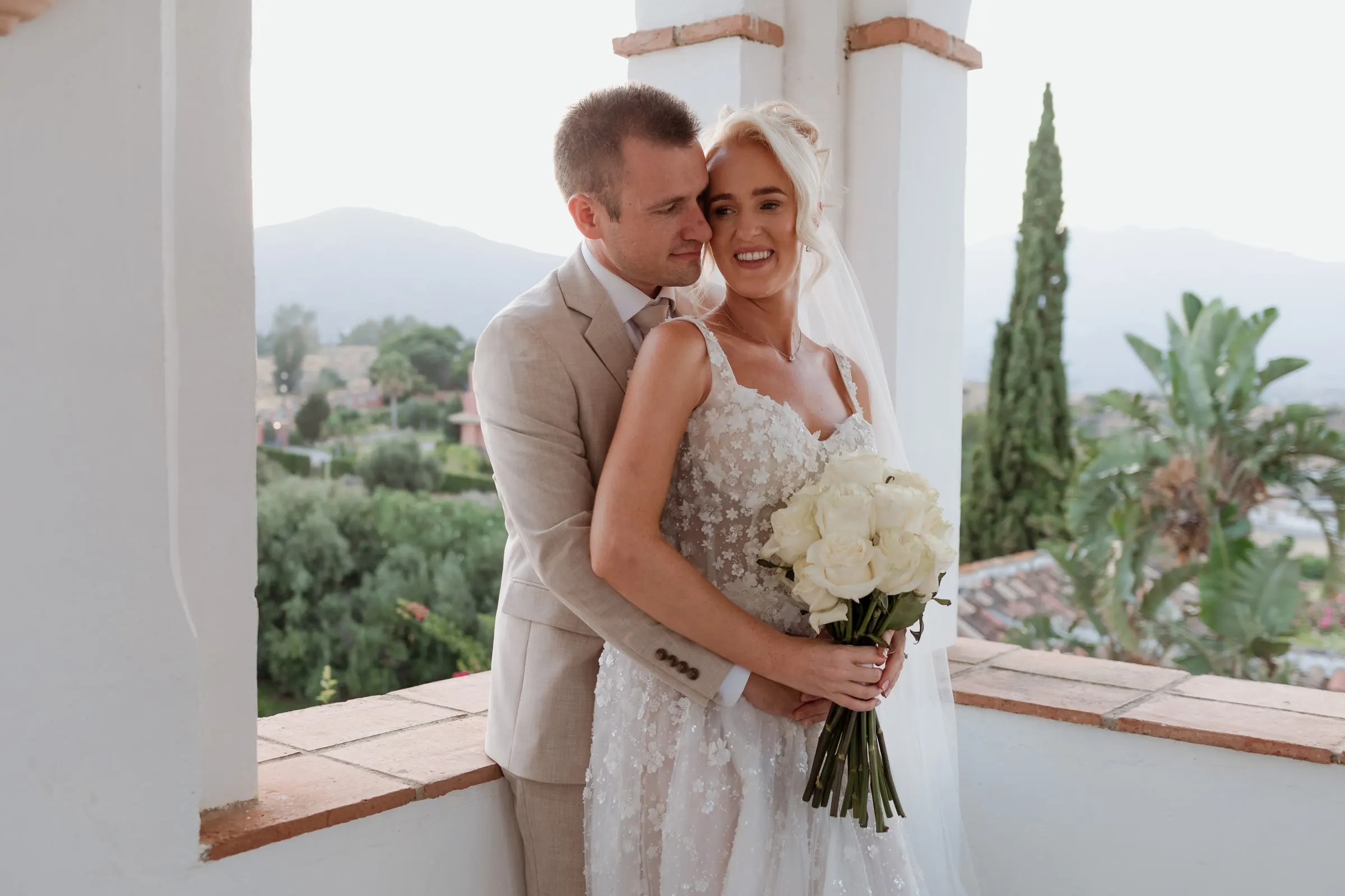 Bride and groom close together in the tower loggia with palm trees behind