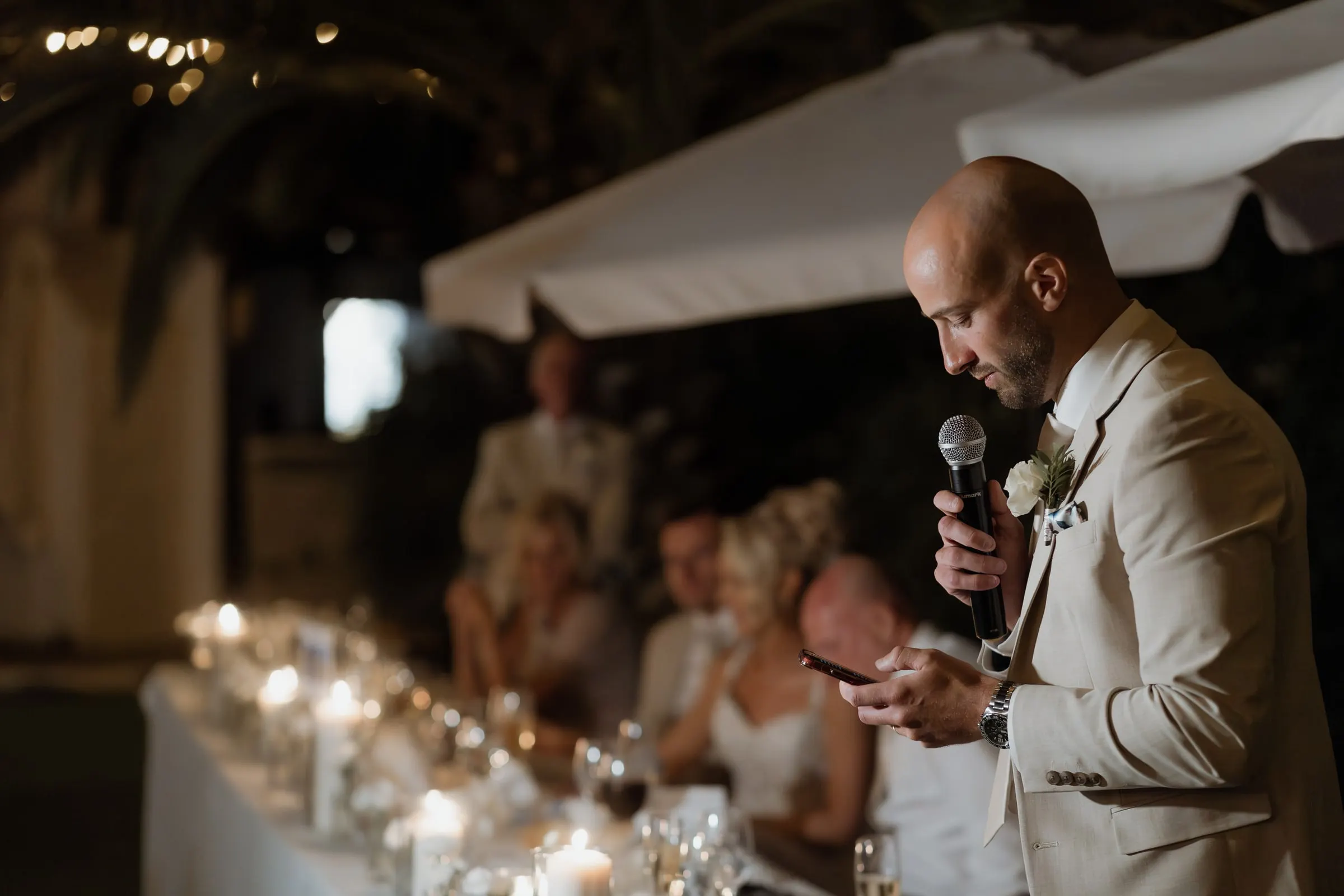 Best man reading his speech from his phone under the parasols