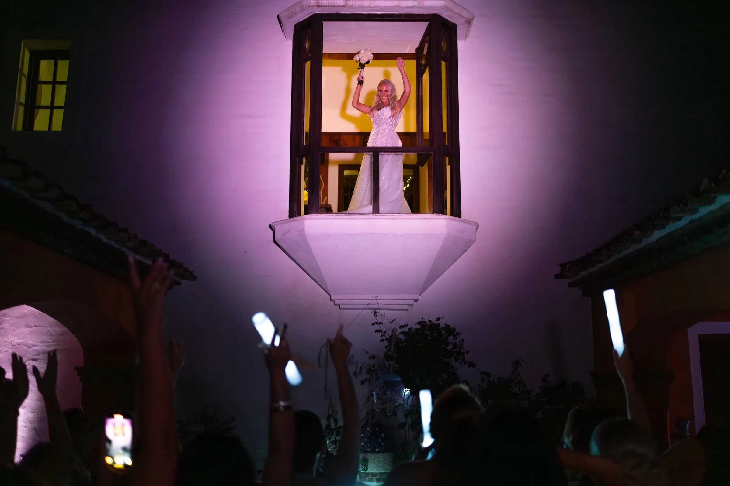 Bride singing from a lit balcony window above the guests with glow sticks, Hacienda San José