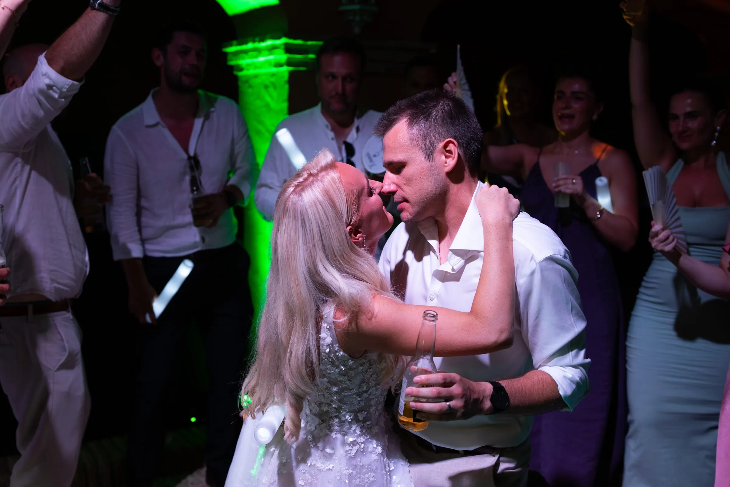 Groom kissing the bride on the dance floor under green lights