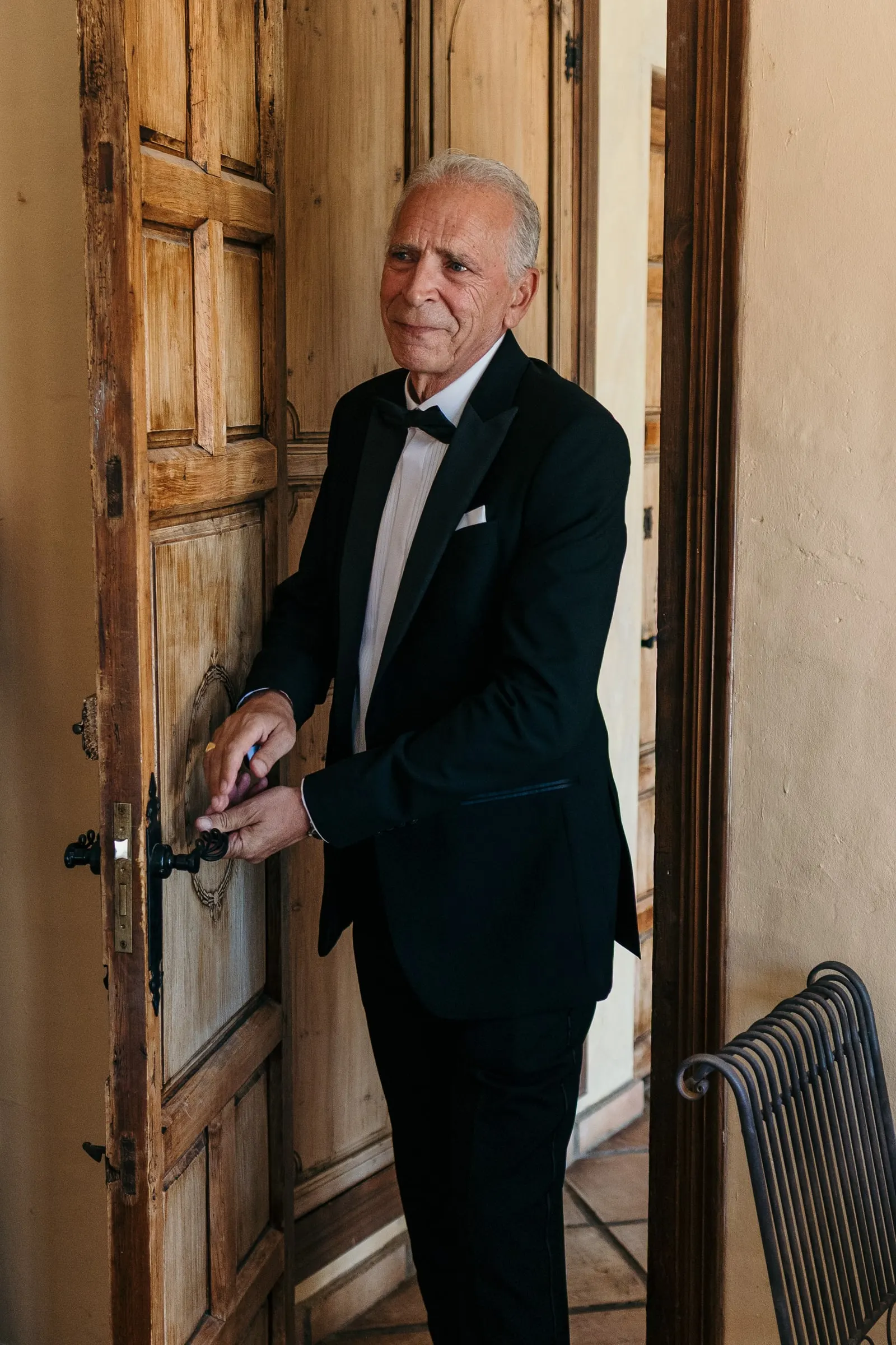 Father of the bride in a tuxedo opening a wooden door at the hacienda