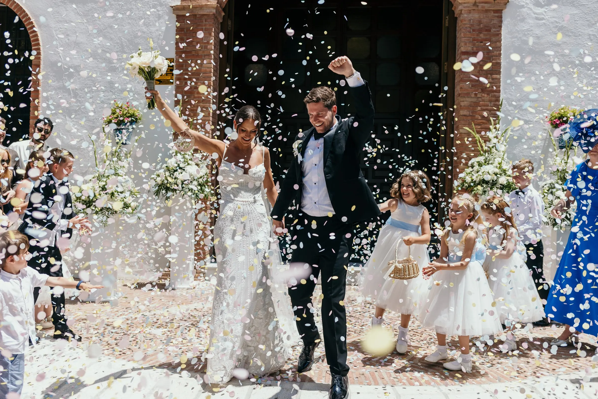 Los novios levantan las manos mientras los invitados lanzan pétalos en Mijas Pueblo