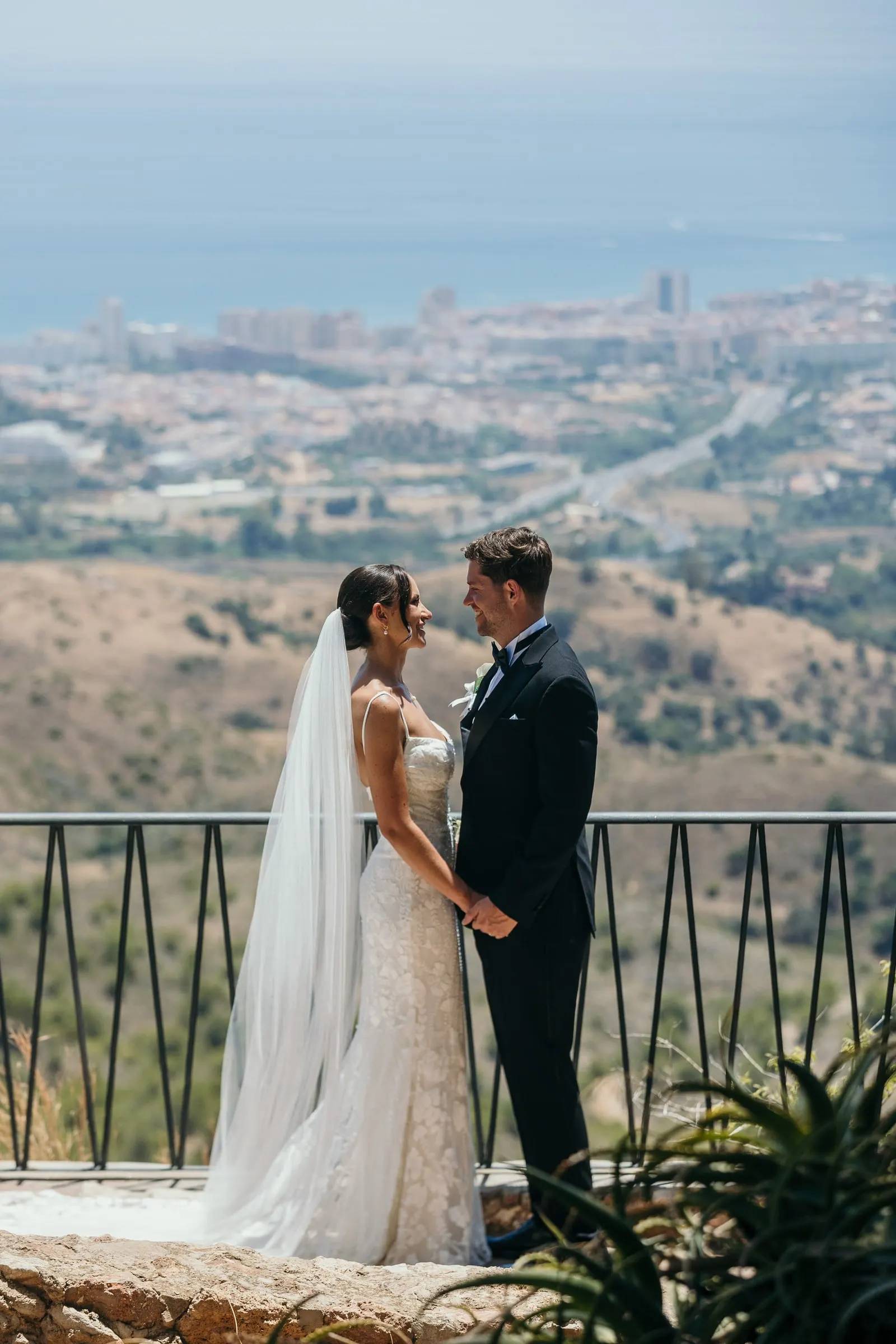 Bride and groom at the railing with the coast and the sea below Mijas