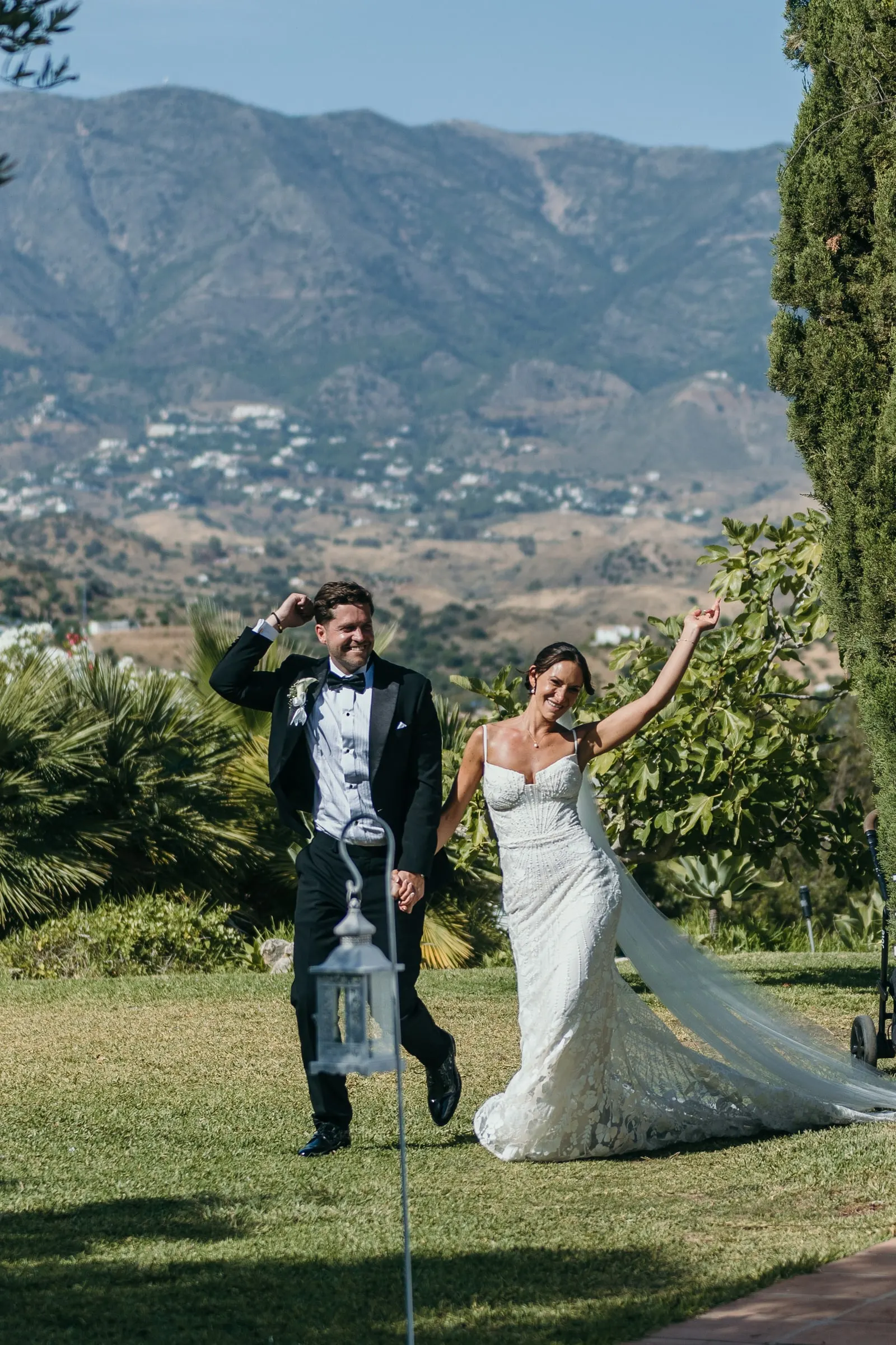 Bride waving as the couple cross the lawn with the Mijas mountains behind