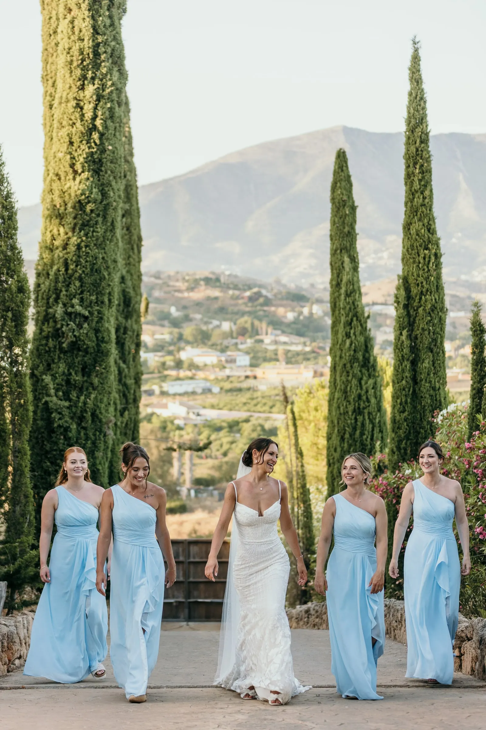Novia y damas de honor por el paseo de cipreses de Hacienda San José con la sierra al fondo