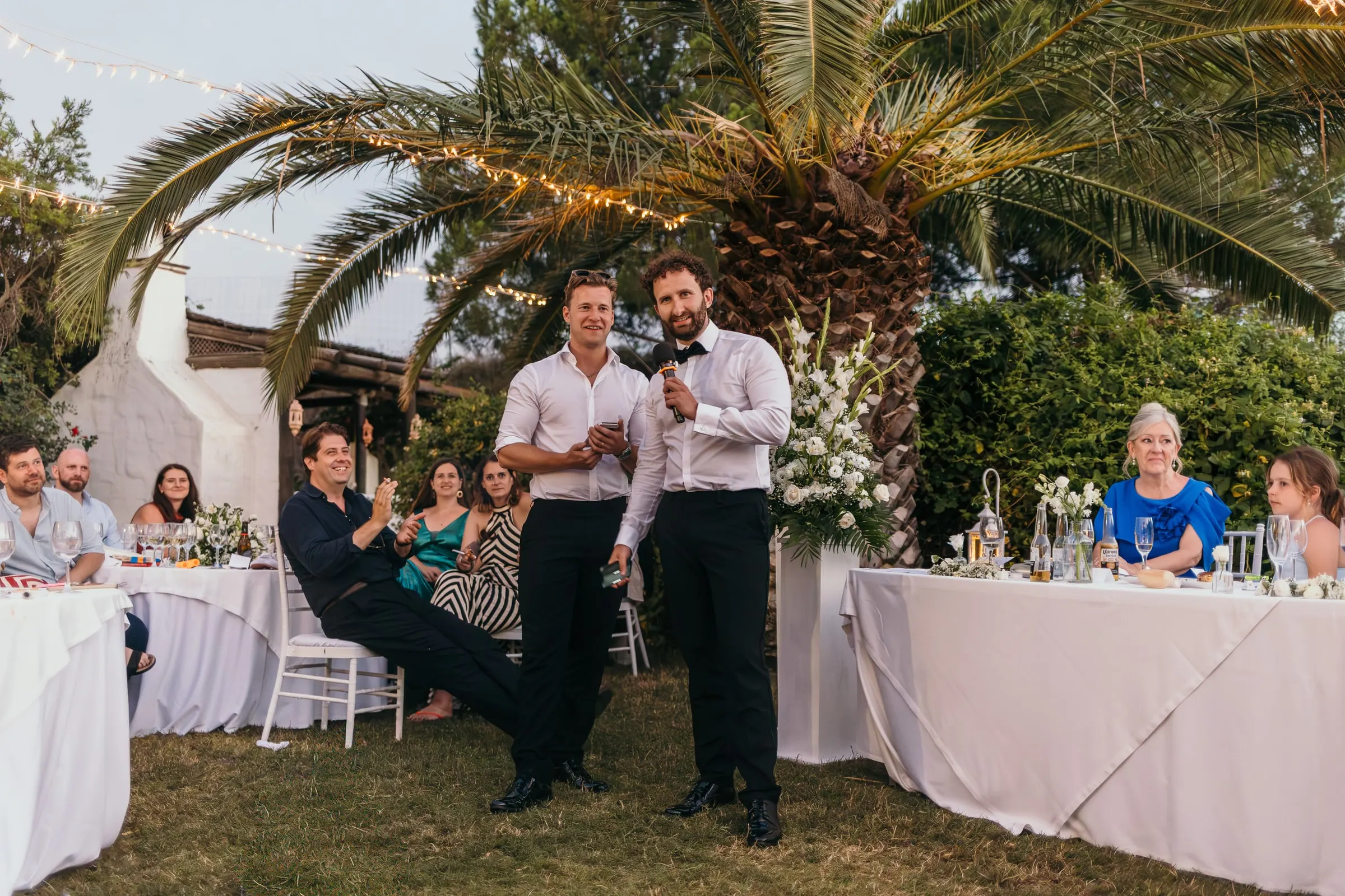 Guests talking at long tables under the palms at the evening reception
