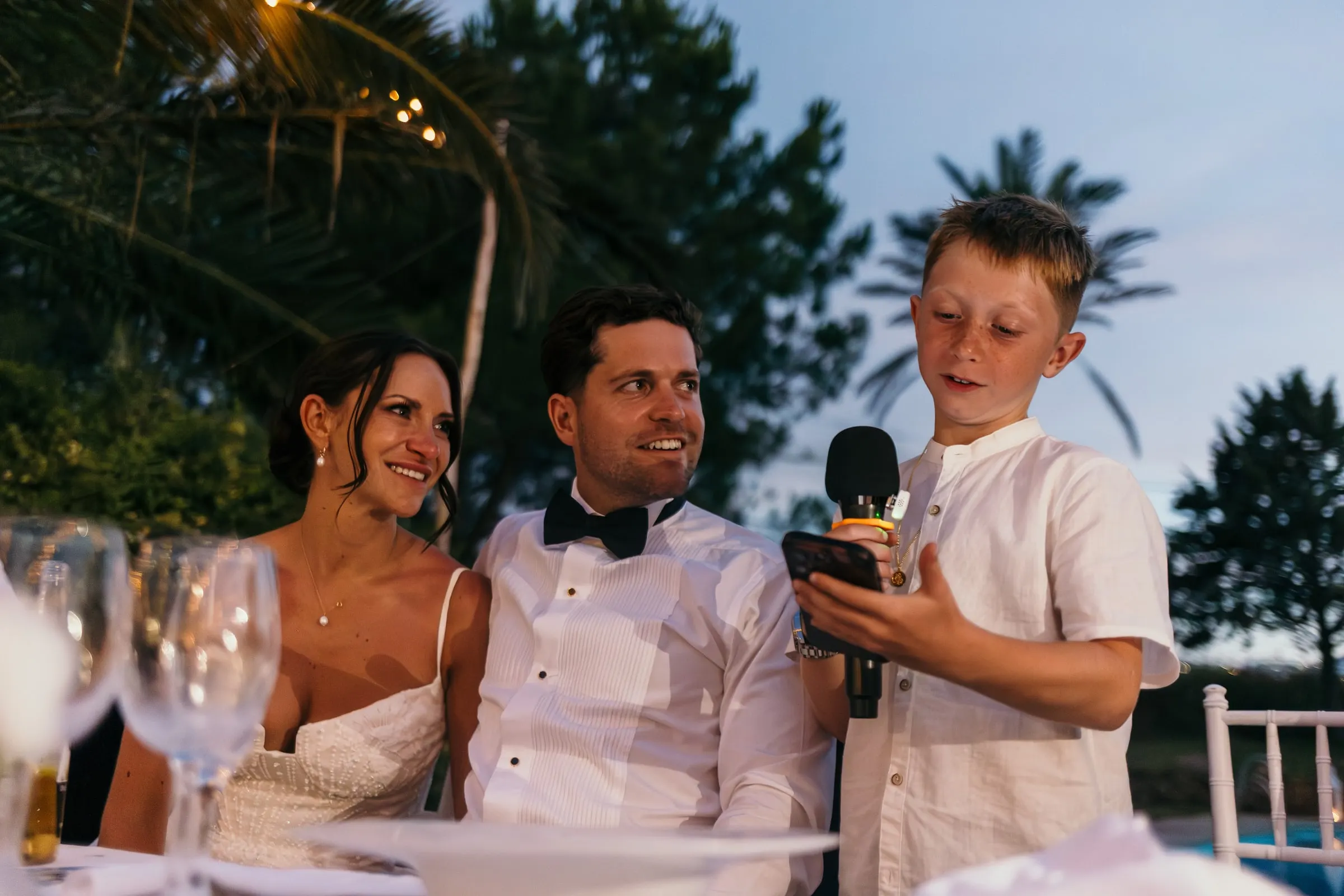Bride and groom laughing as a young guest speaks into the microphone