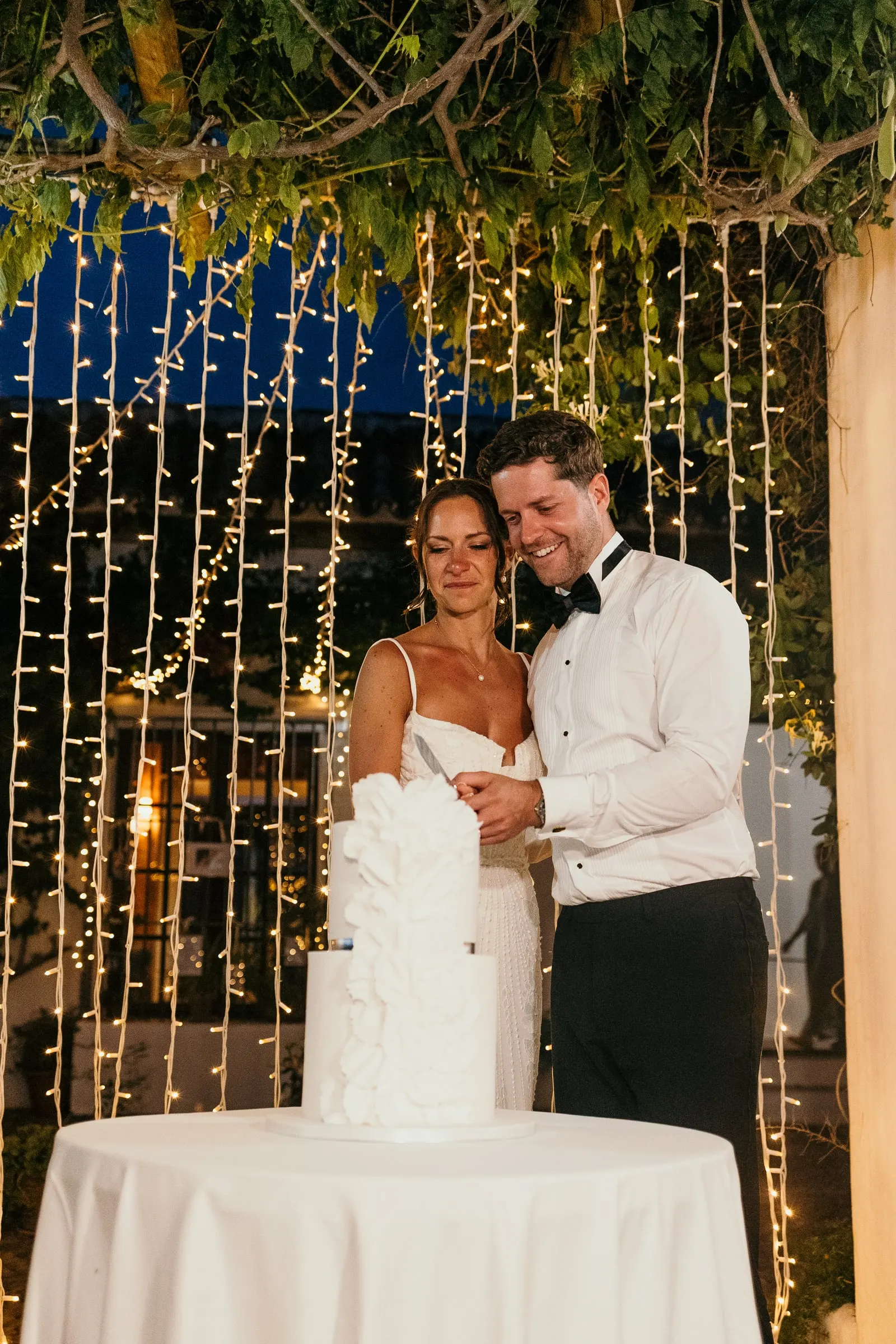Couple cutting the wedding cake under a curtain of lights