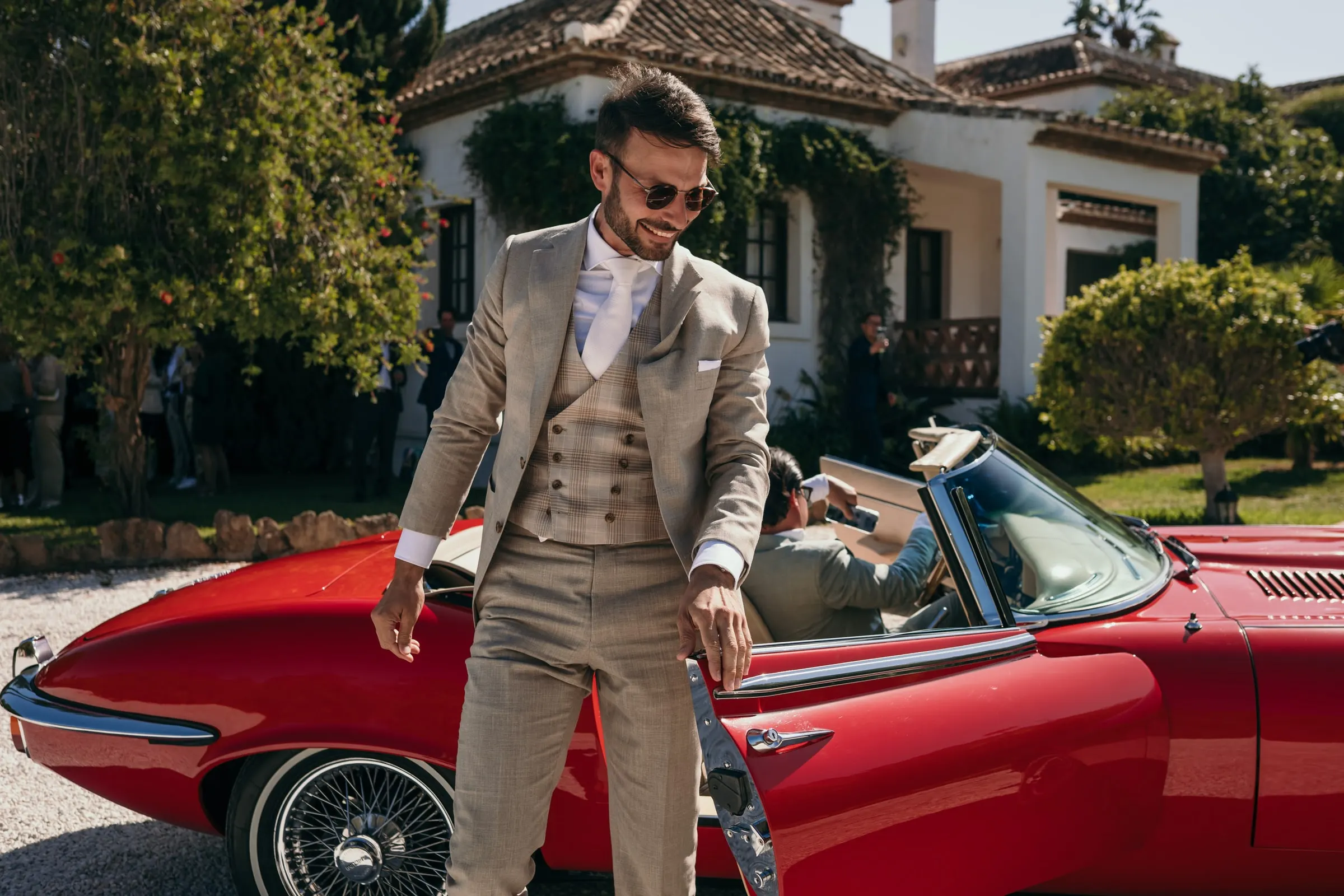 El novio, con traje beis de tres piezas, baja de un descapotable rojo antiguo, Hacienda San José, Mijas