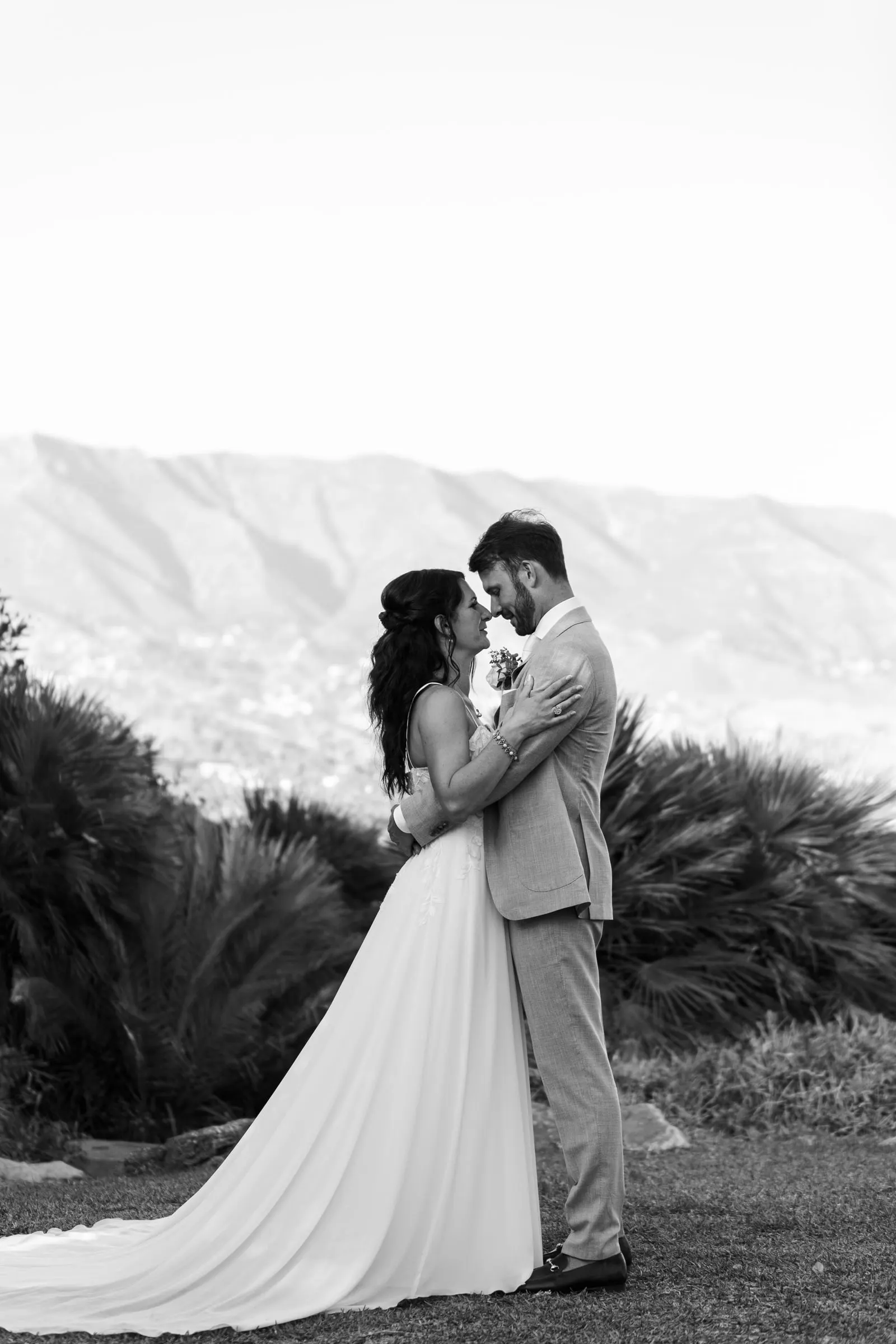 Los novios abrazados en blanco y negro en una ladera con las montañas detrás, Hacienda San José, Mijas