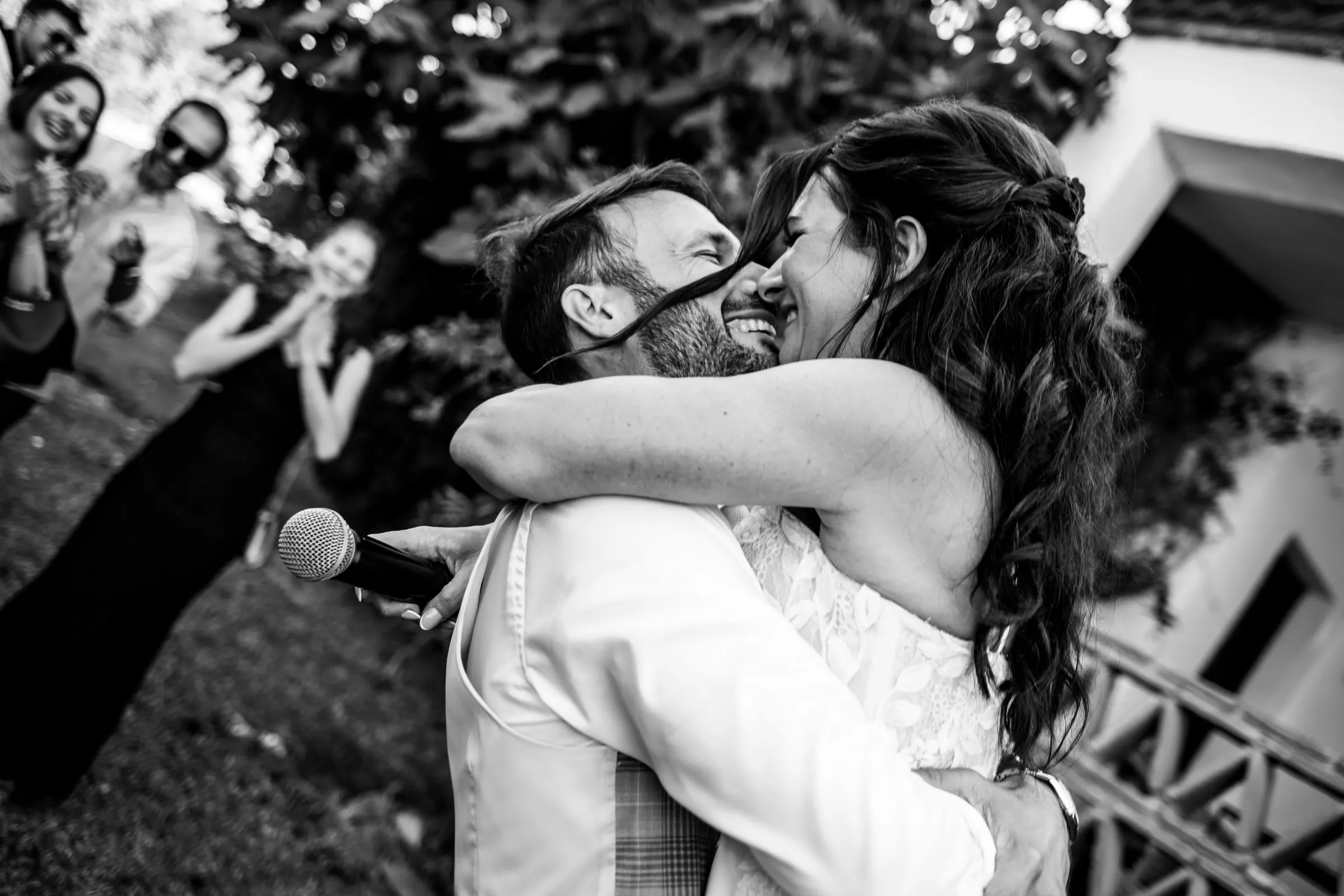Los novios se abrazan con fuerza en blanco y negro mientras los invitados ríen, Hacienda San José, Mijas