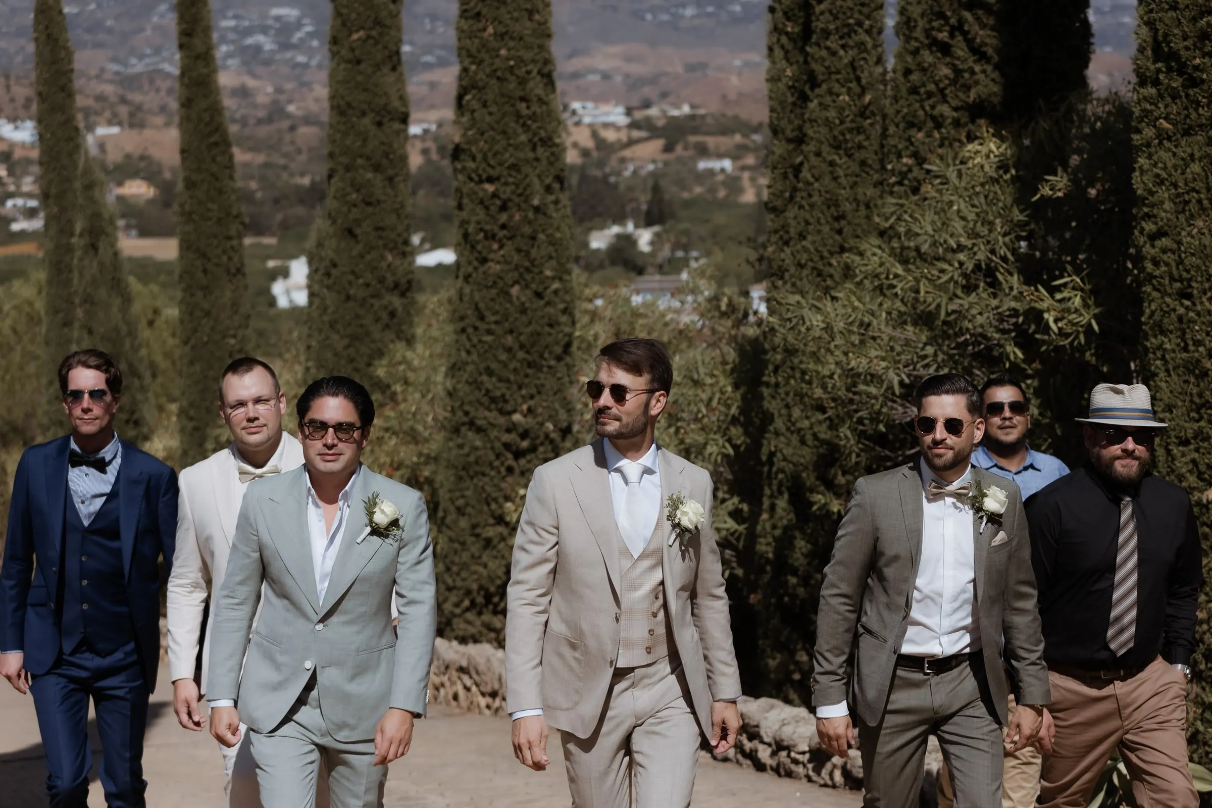 El novio y sus amigos avanzan con trajes de verano por un camino flanqueado de cipreses, Hacienda San José, Mijas
