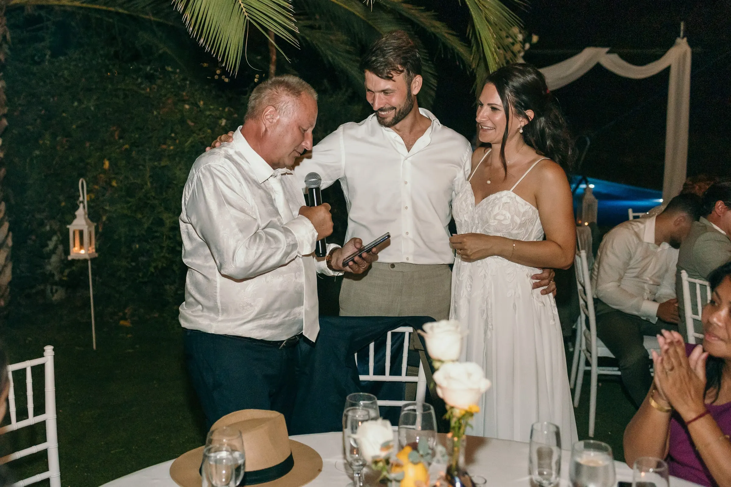 Un invitado da un discurso con micrófono junto a los recién casados sonrientes de noche, Hacienda San José, Mijas