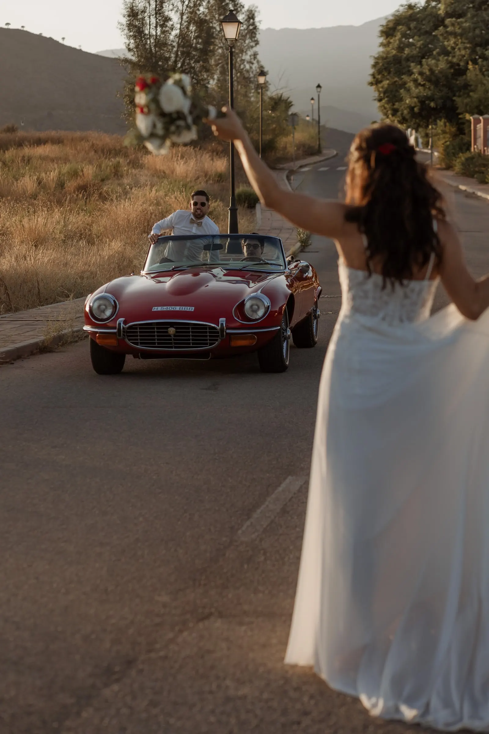 La novia agita el ramo en la carretera mientras el novio llega en un descapotable rojo, Hacienda San José, Mijas