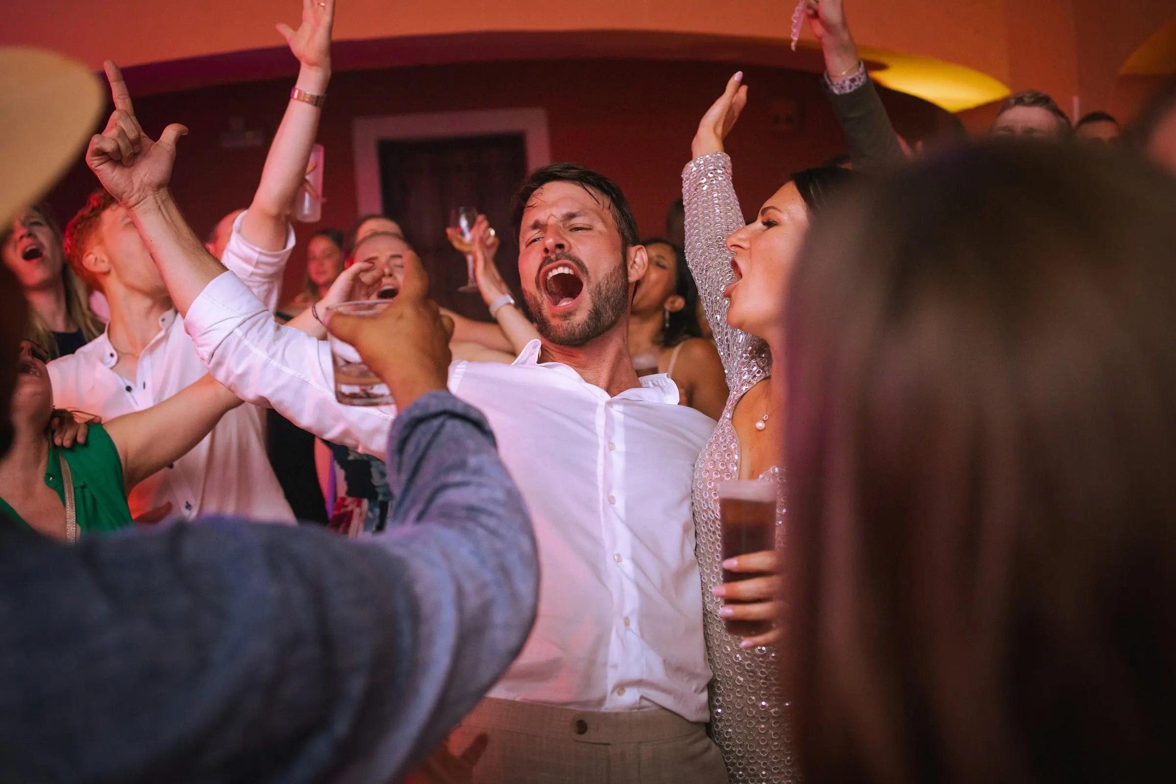 El novio canta con los invitados mientras se alzan las manos en una pista llena y roja, Hacienda San José, Mijas