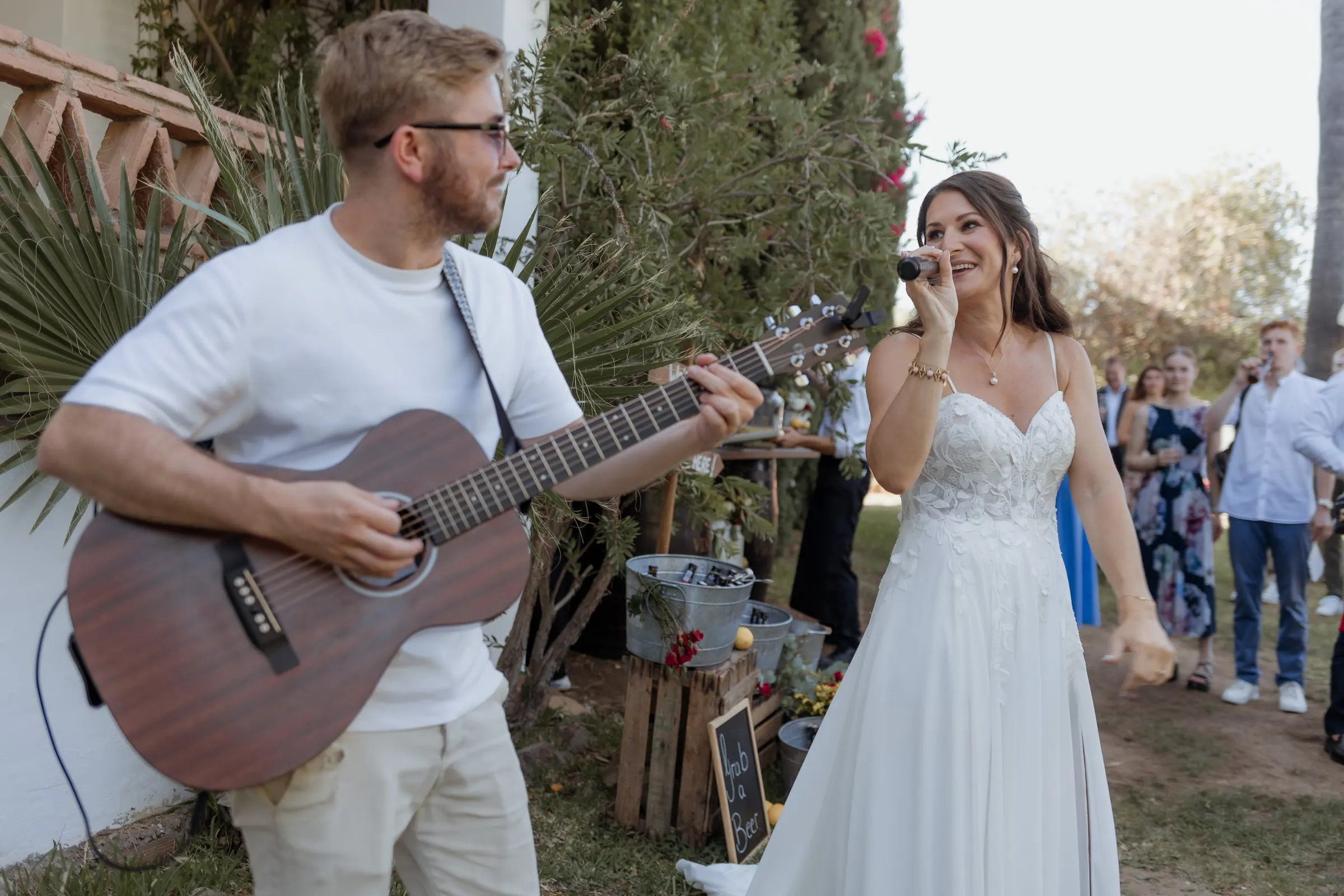 La novia canta al micrófono mientras un invitado toca la guitarra en el jardín, Hacienda San José, Mijas