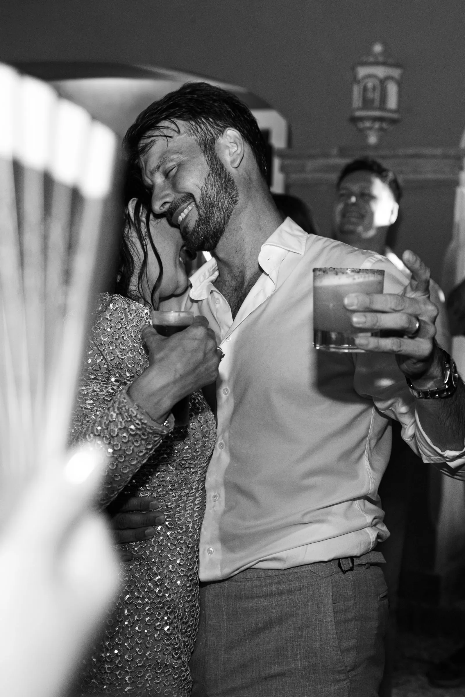 El novio se ríe con una copa en la mano junto a una invitada que baila, en blanco y negro, Hacienda San José, Mijas