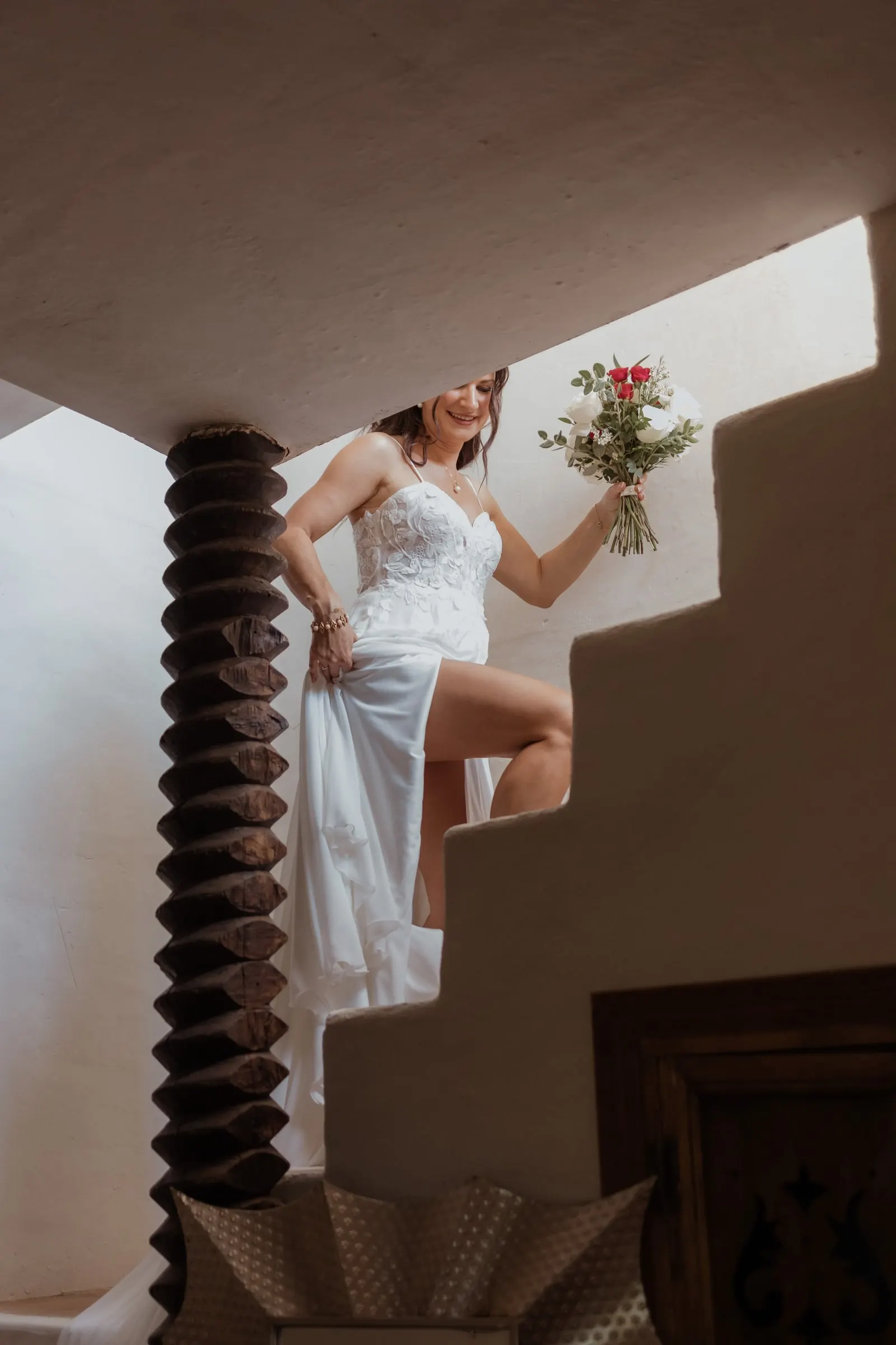 La novia sube una escalera blanca con el ramo, recogiéndose el vestido, Hacienda San José, Mijas
